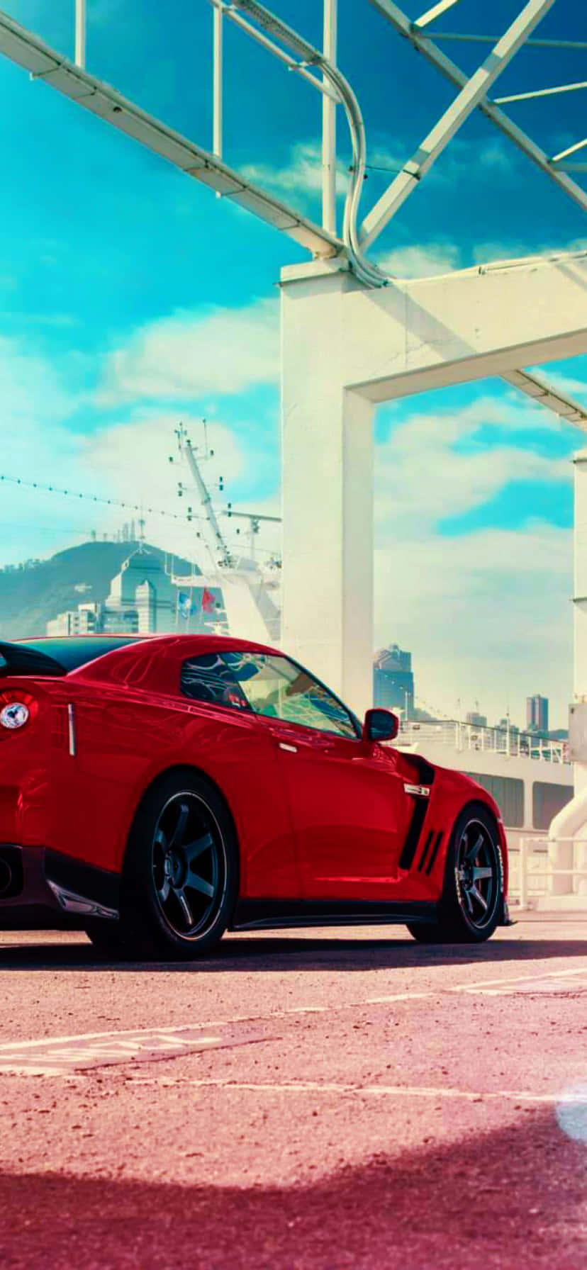 動漫風格 Nissan R35 GT-R 車款 壁紙 — 一輛鮮紅色跑車停泊在白色橋樑下，背景是城市天際線和山脈，天空湛藍明亮。