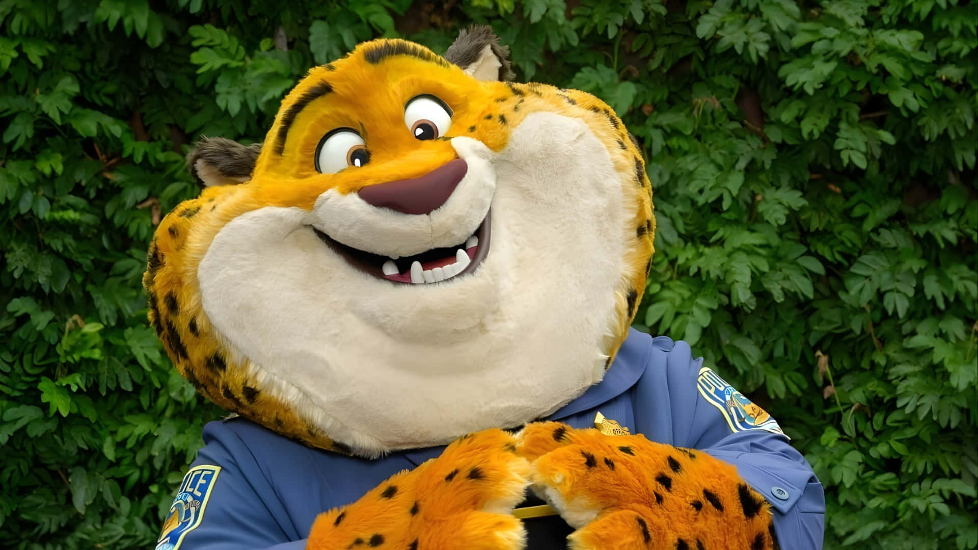 動物方城市 警察 Clawhauser 微笑 壁紙 — 一個穿著藍色警察制服、開心的動畫獵豹吉祥物，在茂密綠色樹葉背景下燦爛地微笑。