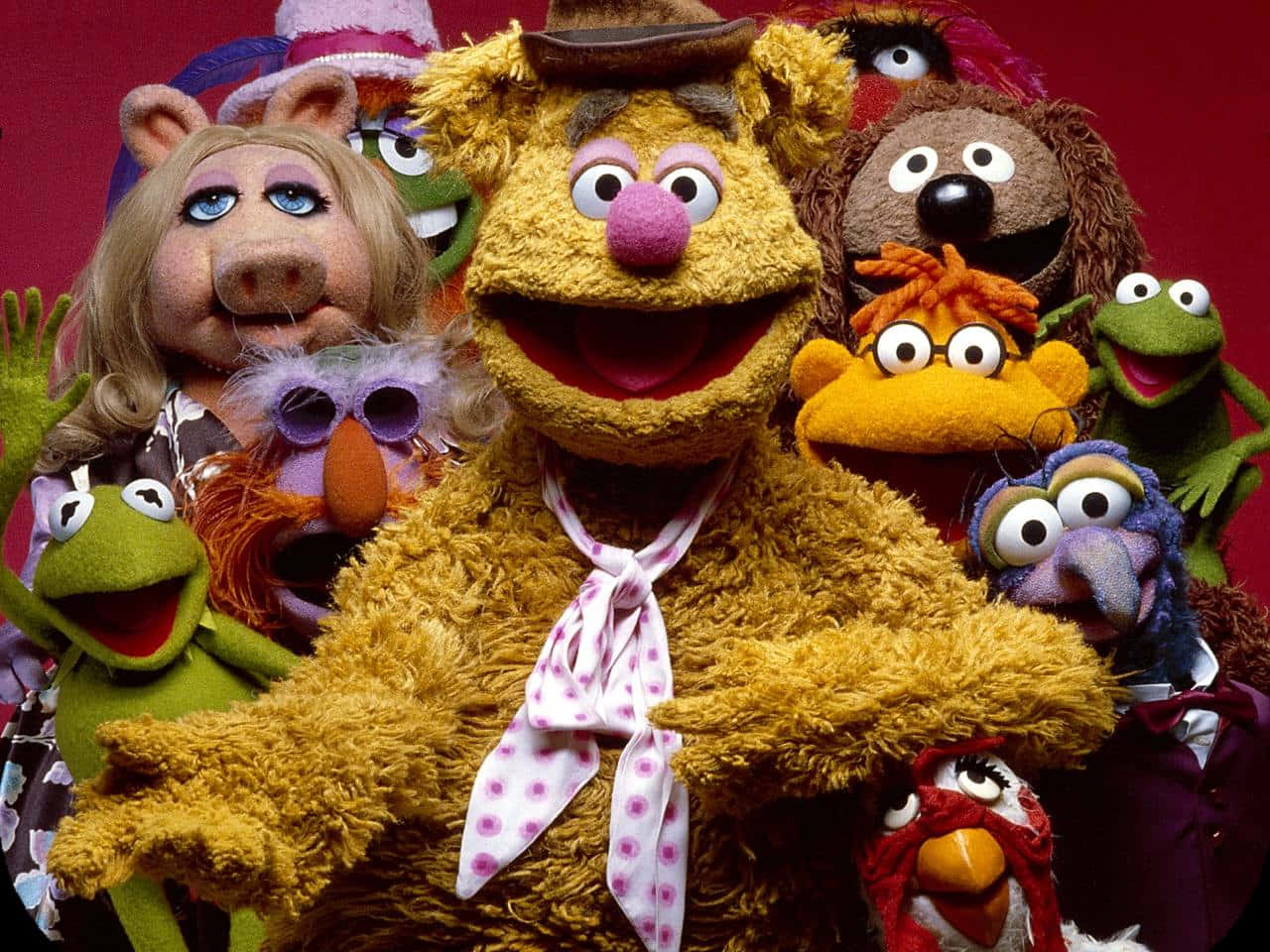 一群開心的Muppet角色一起擺姿勢，帶著燦爛的笑容。