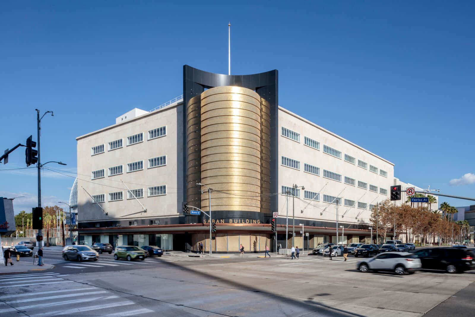 動畫博物館街景圖 壁紙 — 一座引人注目的裝飾藝術風格建築，擁有金色圓柱形塔樓，在晴朗的藍天下高聳，汽車和行人穿梭於繁忙的城市十字路口。