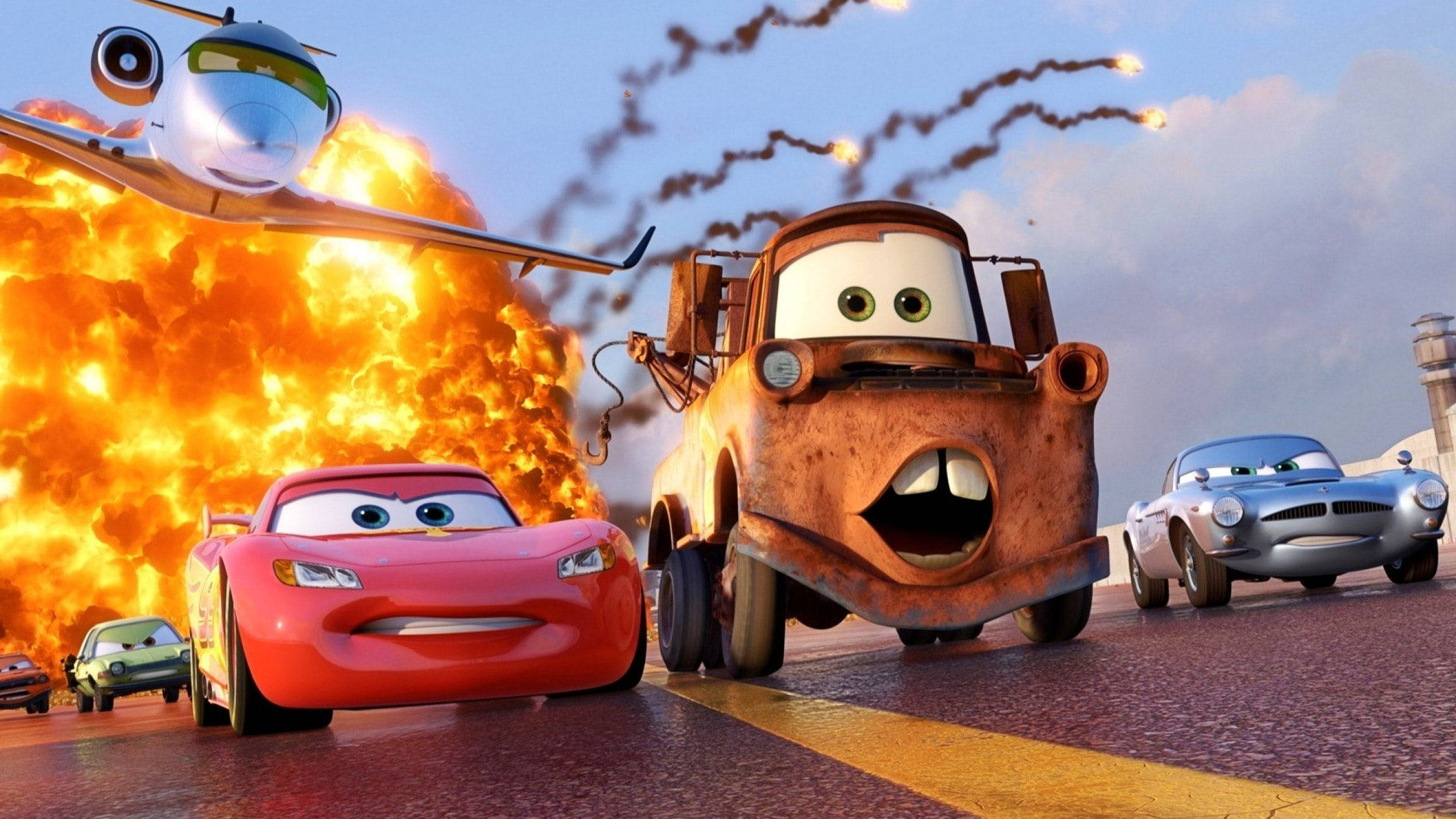 Disney Cars 桌布 壁紙 — 動畫汽車在濕滑的道路上競速，一架飛機在頭頂飛過，伴隨著熾熱的爆炸和煙霧痕跡。