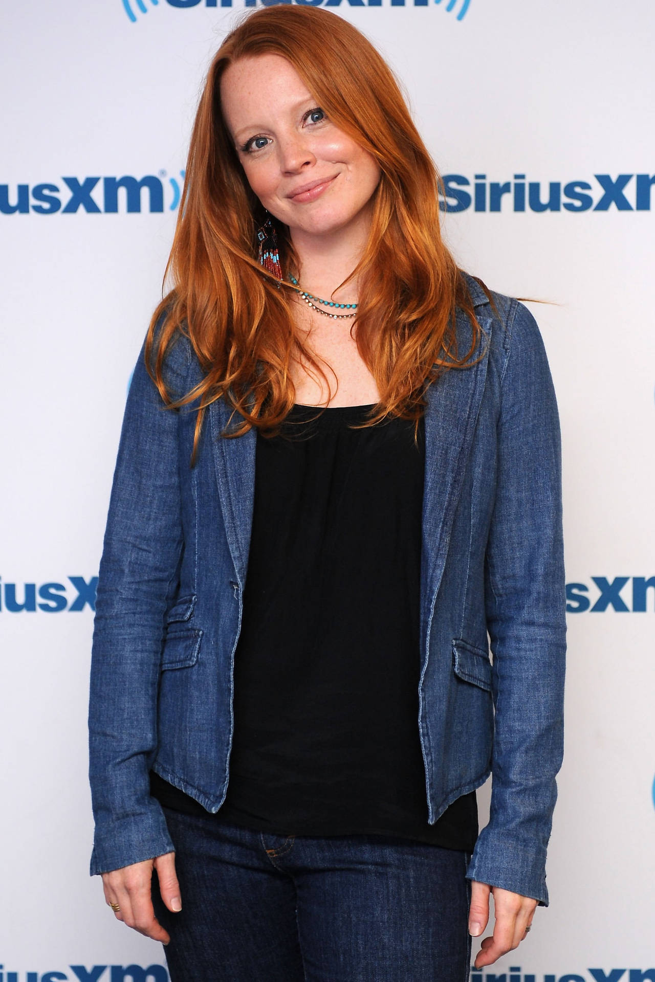 紅髮女性穿牛仔外套在SiriusXM活動中對鏡頭微笑。