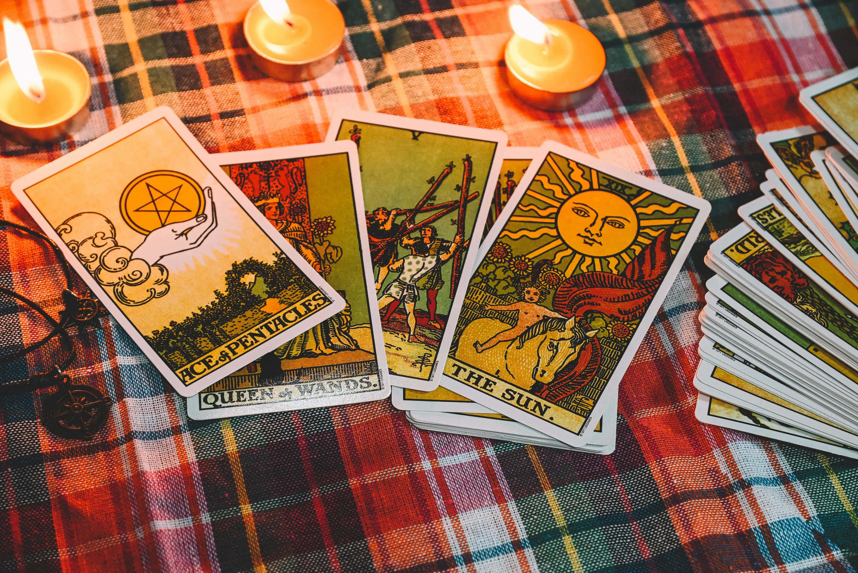 Tarot Card 桌布 壁紙 — 包括「太陽」和「錢幣王牌」在內的塔羅牌放在格仔布上，旁邊點燃的茶燭散發出溫暖的光芒。