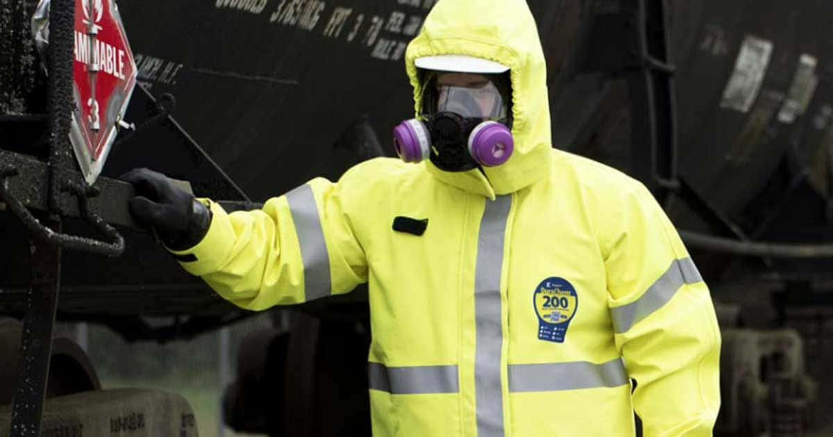 化學安全服圖片 壁紙 — 一名穿著亮黃色防護服和紫色呼吸器的工人在鐵路調車場檢查一節標有「INFECTIOUS」的危險材料車廂。