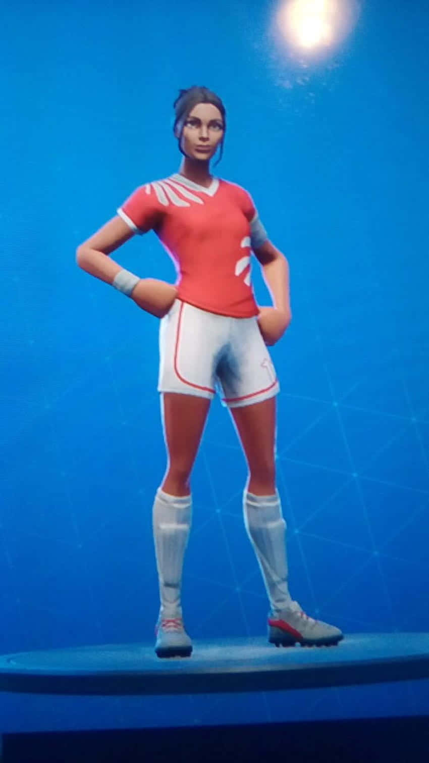 穿著紅白裝備的女性Fortnite足球運動員在藍色平台上擺姿勢。