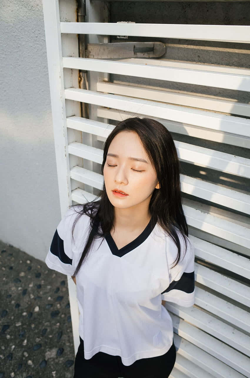 年輕女子在陽光下閉著眼睛靠在白色百葉窗上休息。