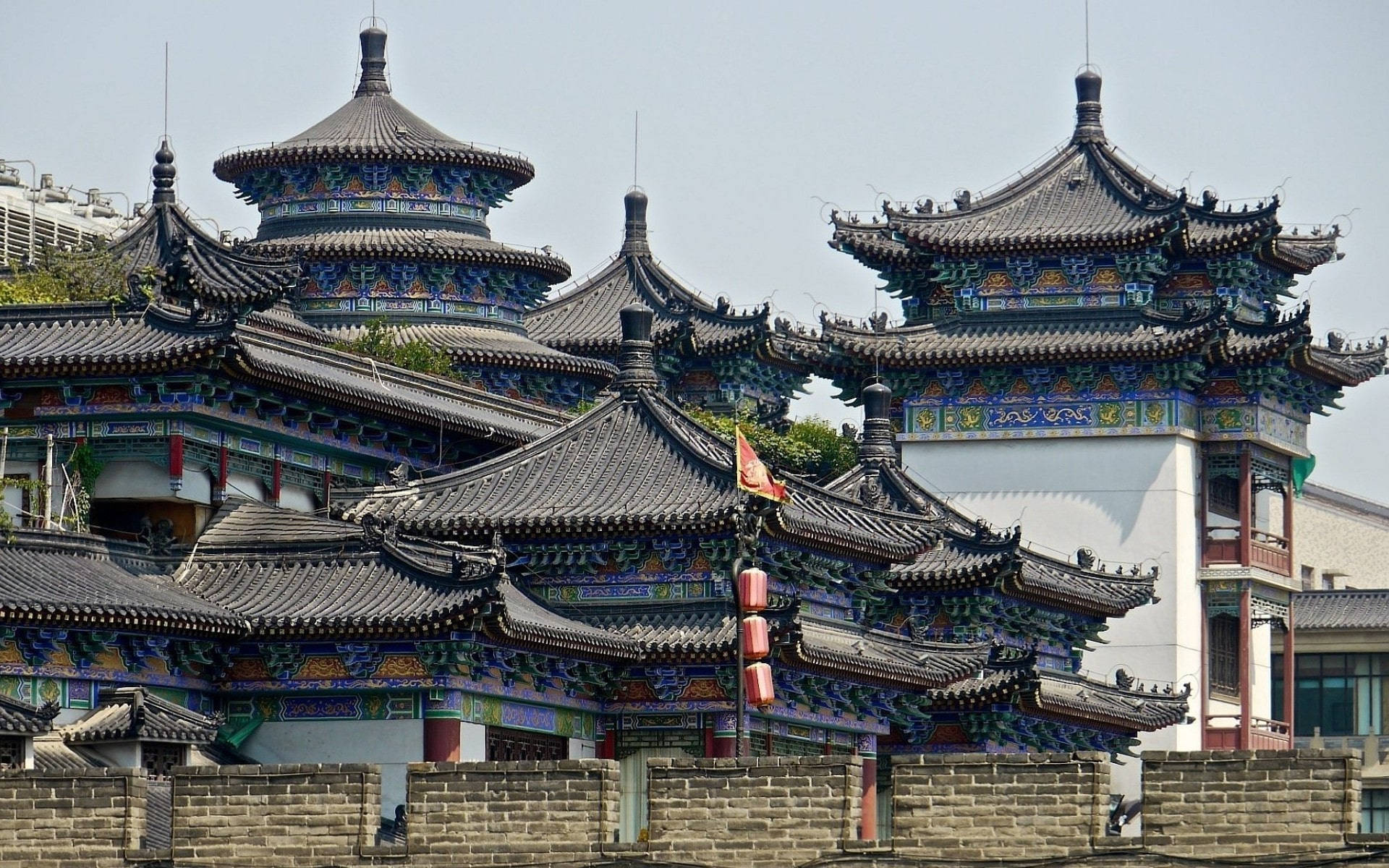 北京宗教廟宇 壁紙 — 傳統中國寺廟屋頂帶有精緻的藍色和金色裝飾，在朦朧的天空下聳立於古老的石牆之上。