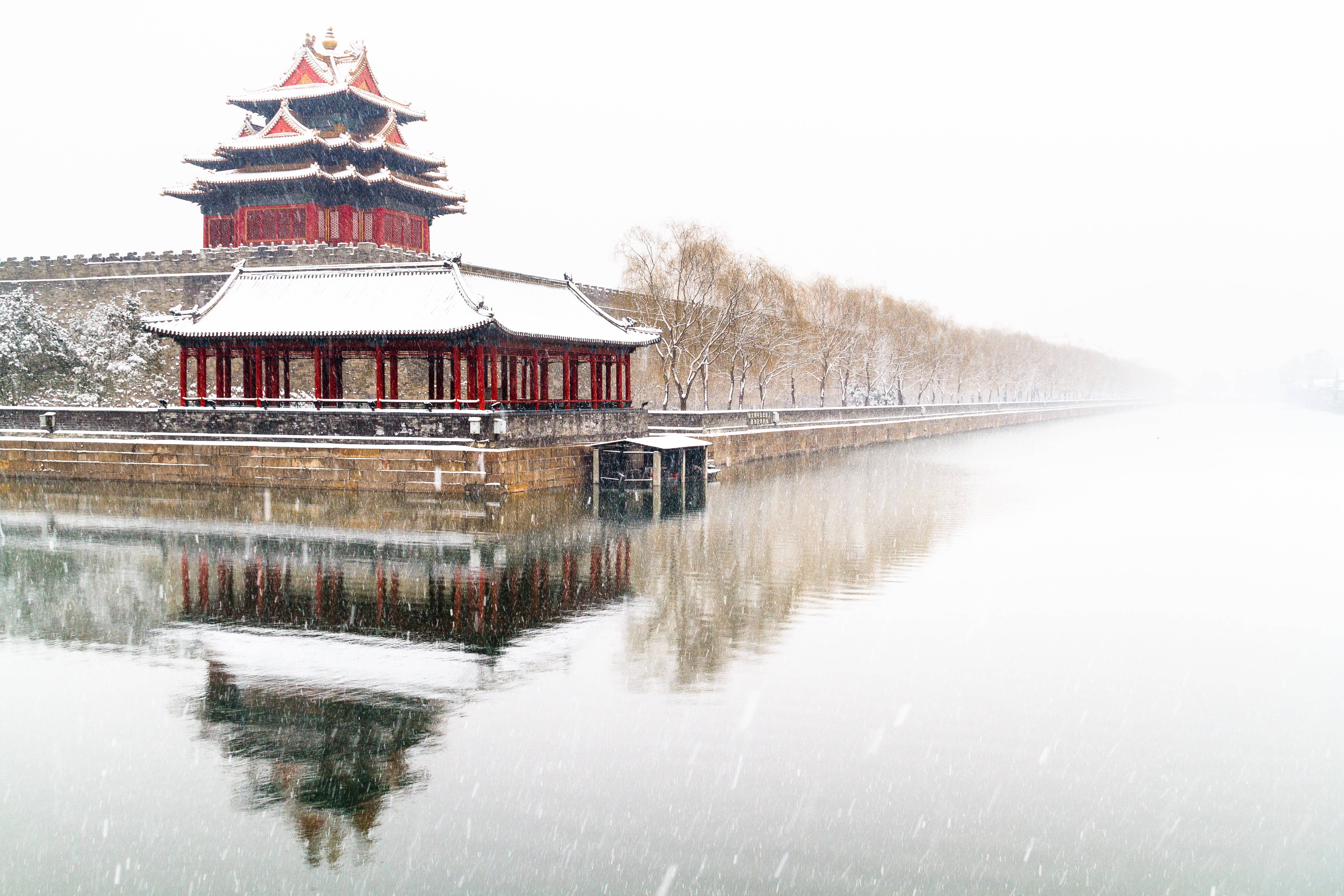 北京故宮雪景 壁紙 — 一個傳統中式亭子，紅色柱子，屋頂積雪，在雪冬季節倒映在平靜的水面上。