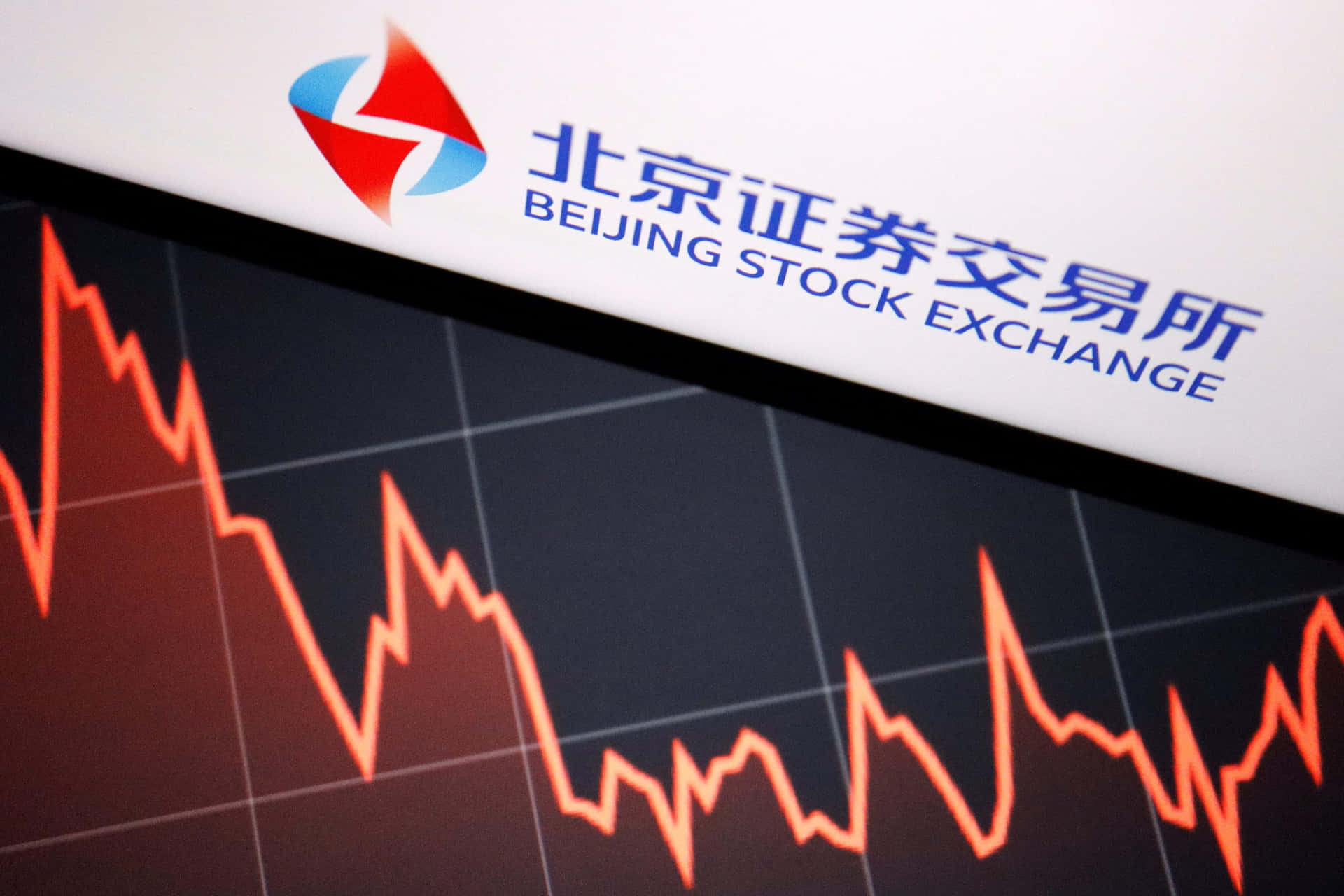 北京證券交易所標誌位於屏幕上顯示下跌的股票市場圖表上方。