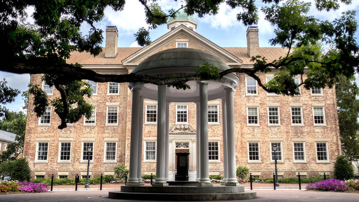 歷史悠久的磚造大學建築，前方有白色柱子和綠色樹木。