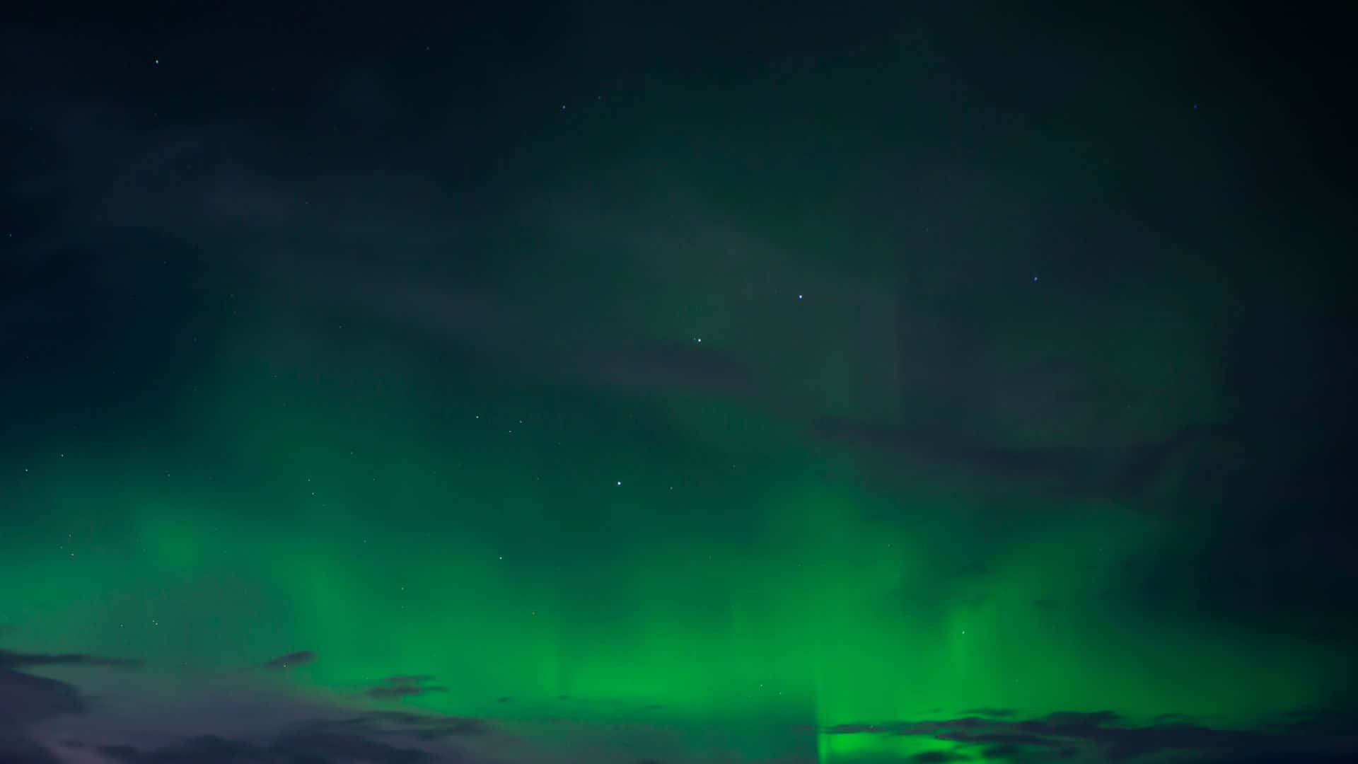 綠色北極光在繁星點點的夜空中閃爍，伴有烏雲。