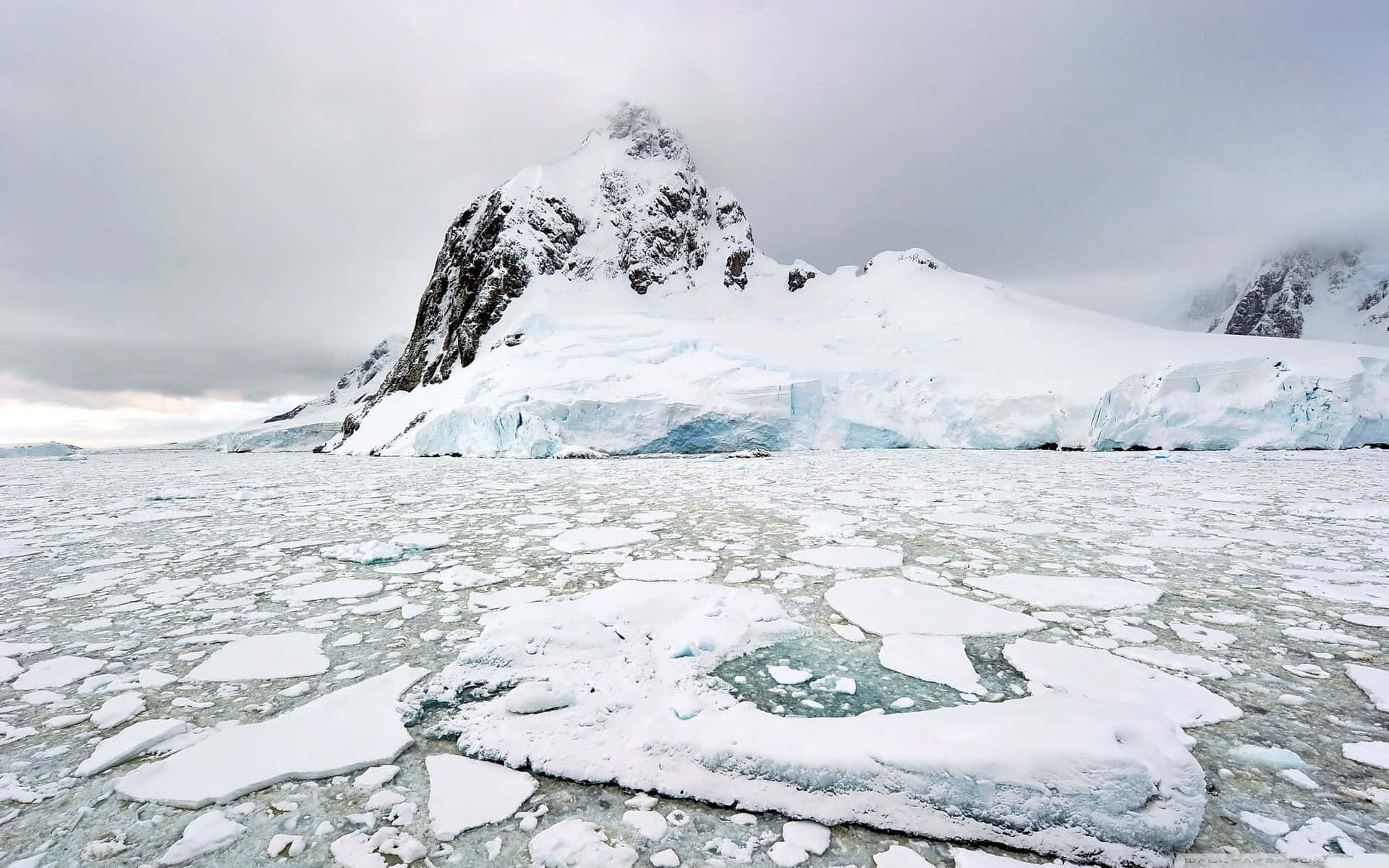 冰凍的海冰碎片在陰天中漂浮在白雪覆蓋的南極山脈前。