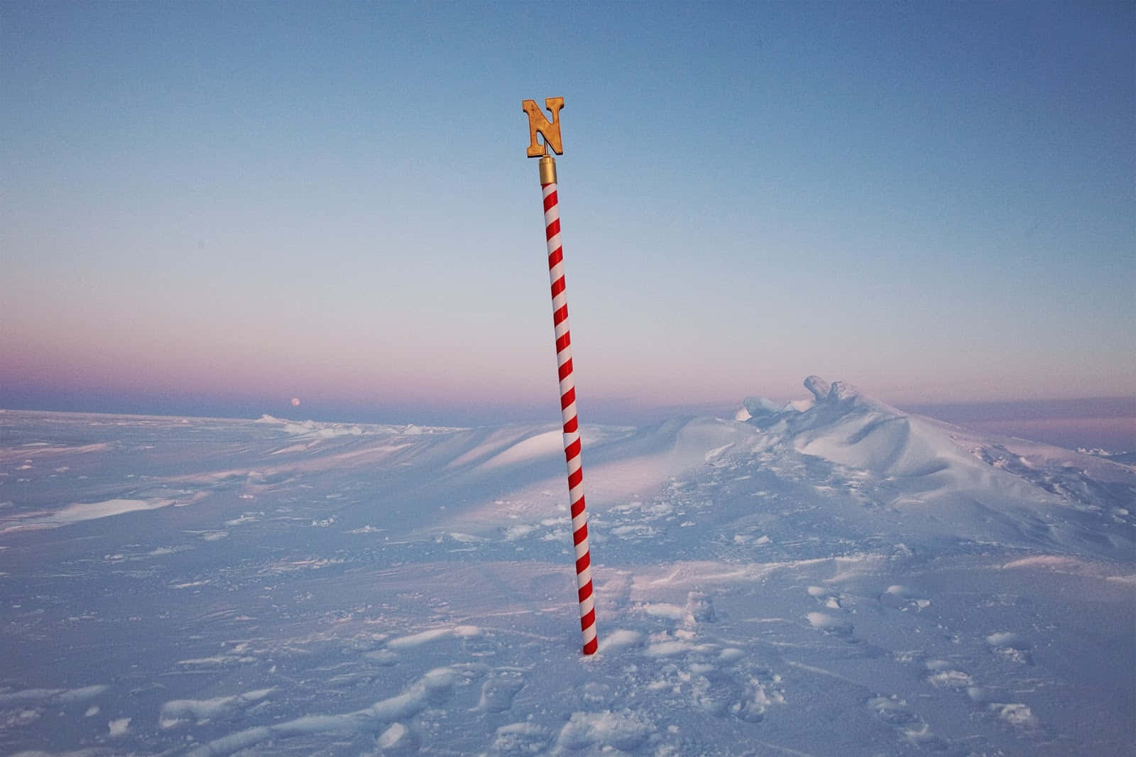 在暮色的雪地北極景觀中，一根紅白條紋的柱子和一個金色的N標記。
