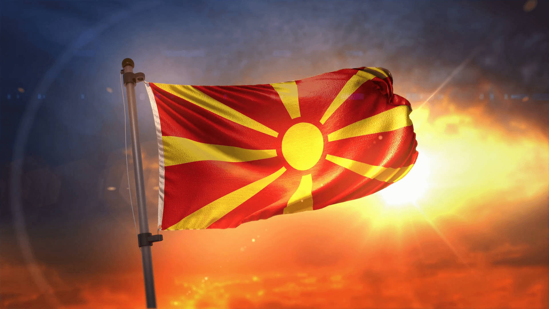 北馬其頓國旗日落時分 壁紙 — 北馬其頓國旗在熾熱的日落天空下自豪地飄揚，伴隨著燦爛的陽光和發光的雲彩。