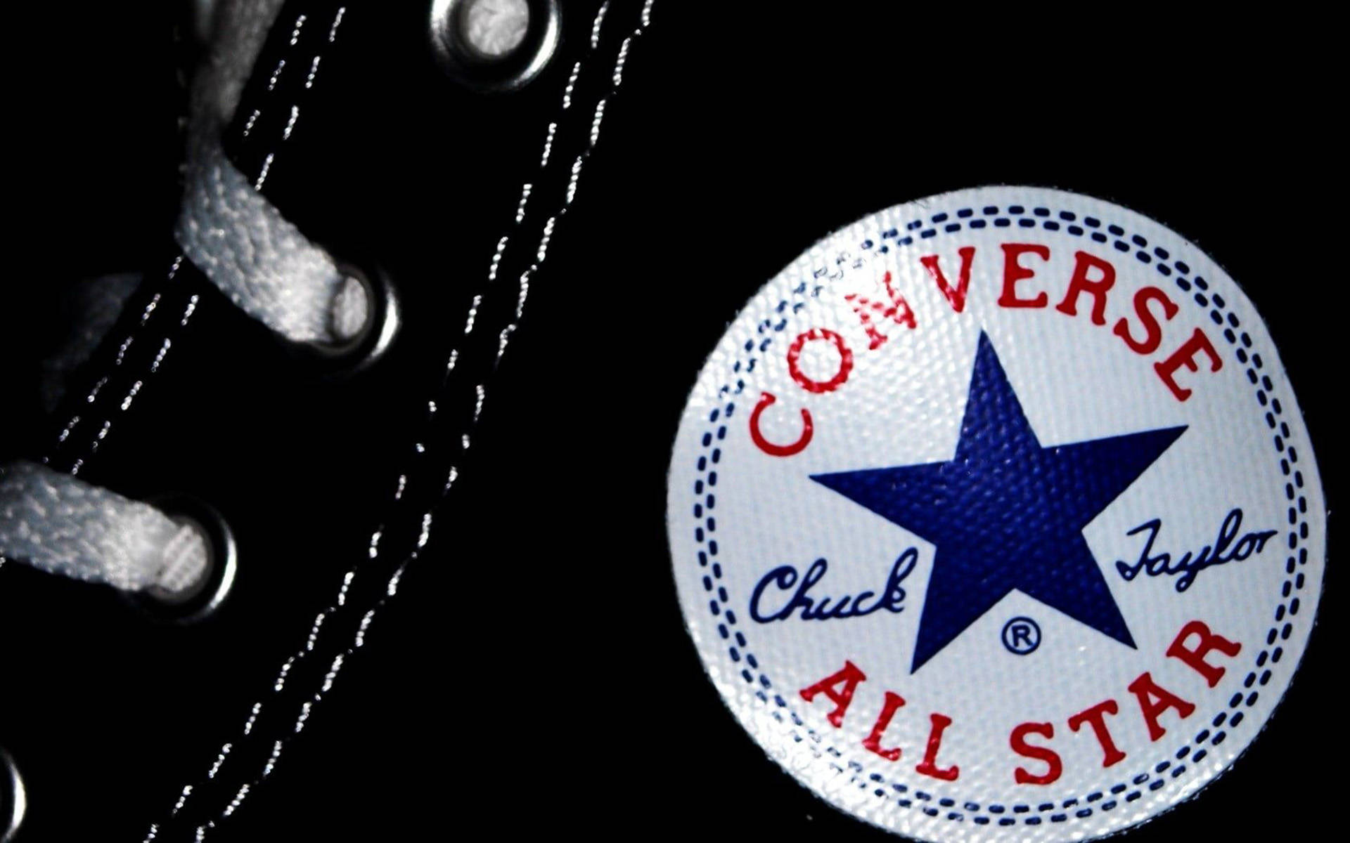 匡威標誌微距特寫 壁紙 — 黑色Converse Chuck Taylor All Star運動鞋標誌性標誌和鞋帶在深色背景下的特寫。
