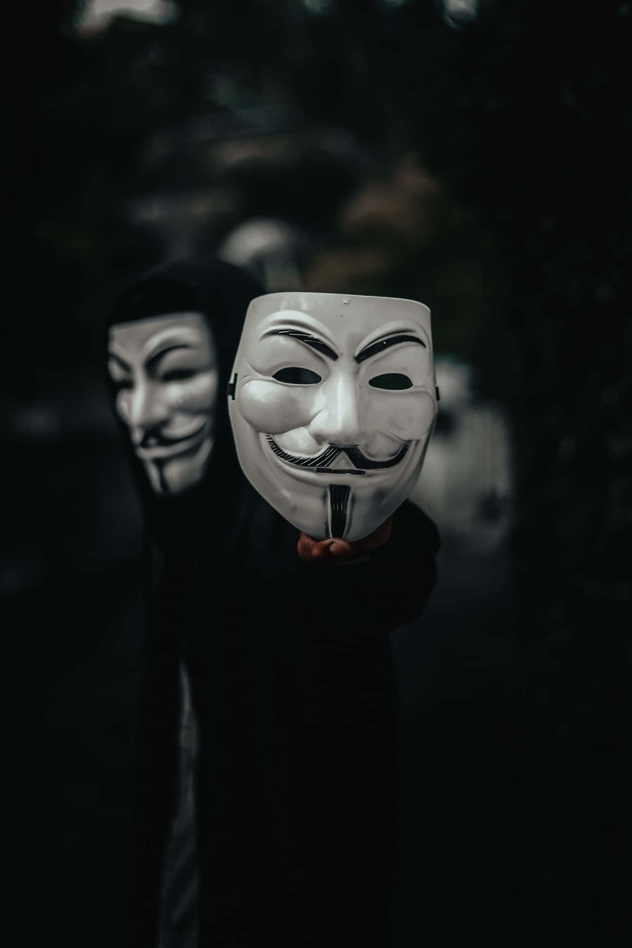 在黑暗環境中手持白色蓋伊·福克斯面具的人。