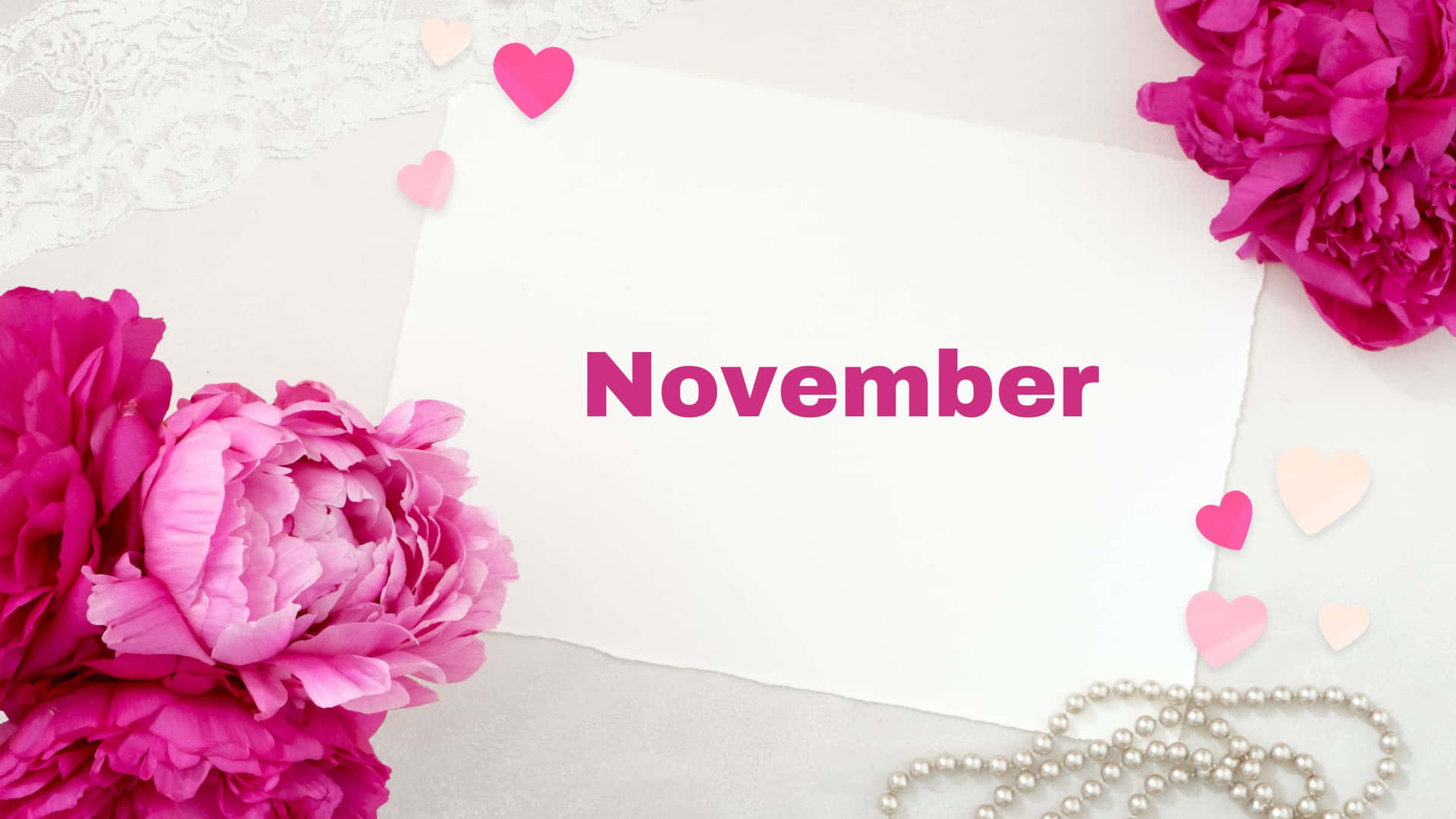 粉紅色牡丹、蕾絲、珍珠和心形圖案圍繞著一張帶有「November」文字的白色卡片。