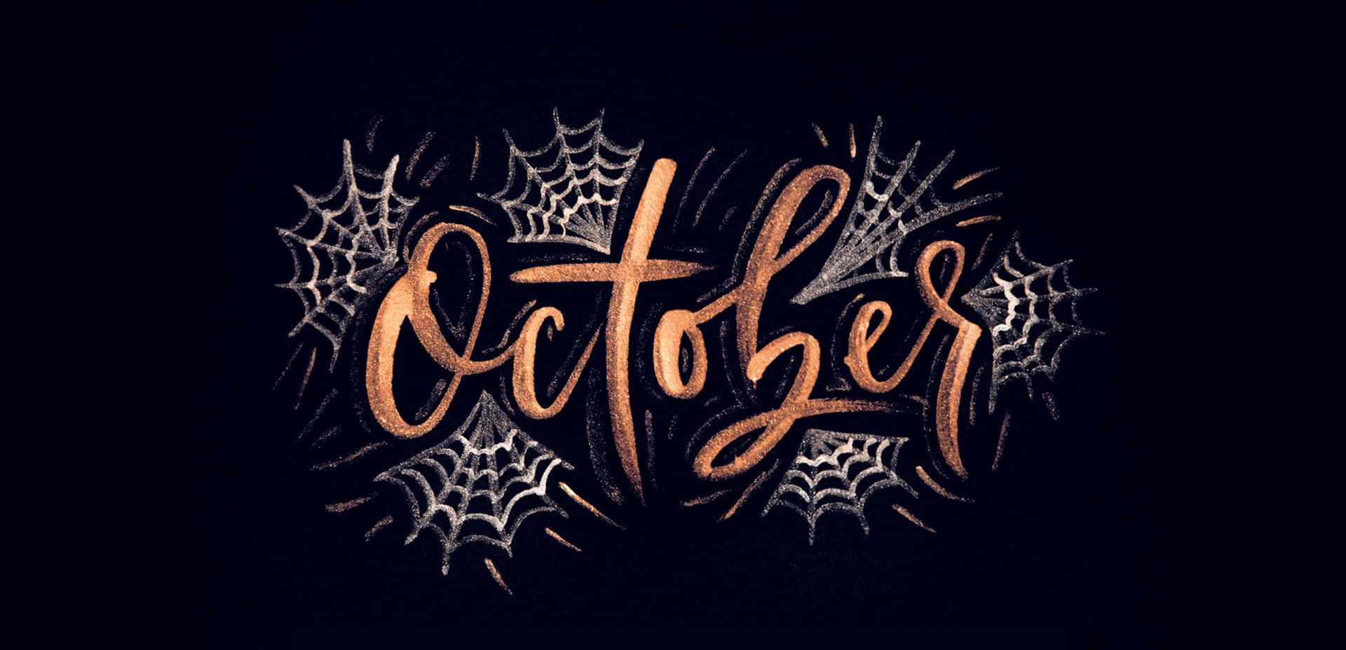 十月，盡享絢爛橙紅葉色之美！ 壁紙 — 在深色背景上，閃閃發光的銅色字體寫著「十月」，周圍環繞著銀色蜘蛛網。
