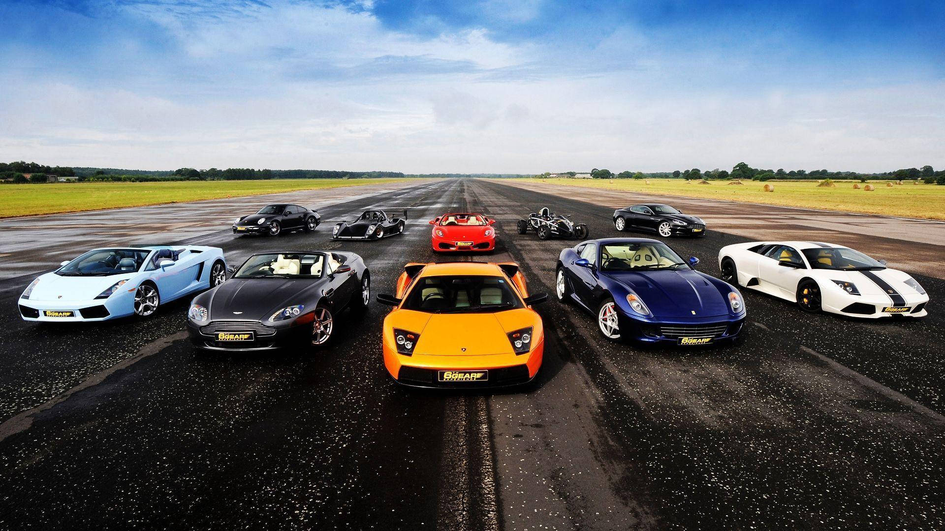 Sports Car 桌布 壁紙 — 十輛色彩鮮豔的高性能跑車排列在潮濕的跑道上，上方是明亮的藍天。