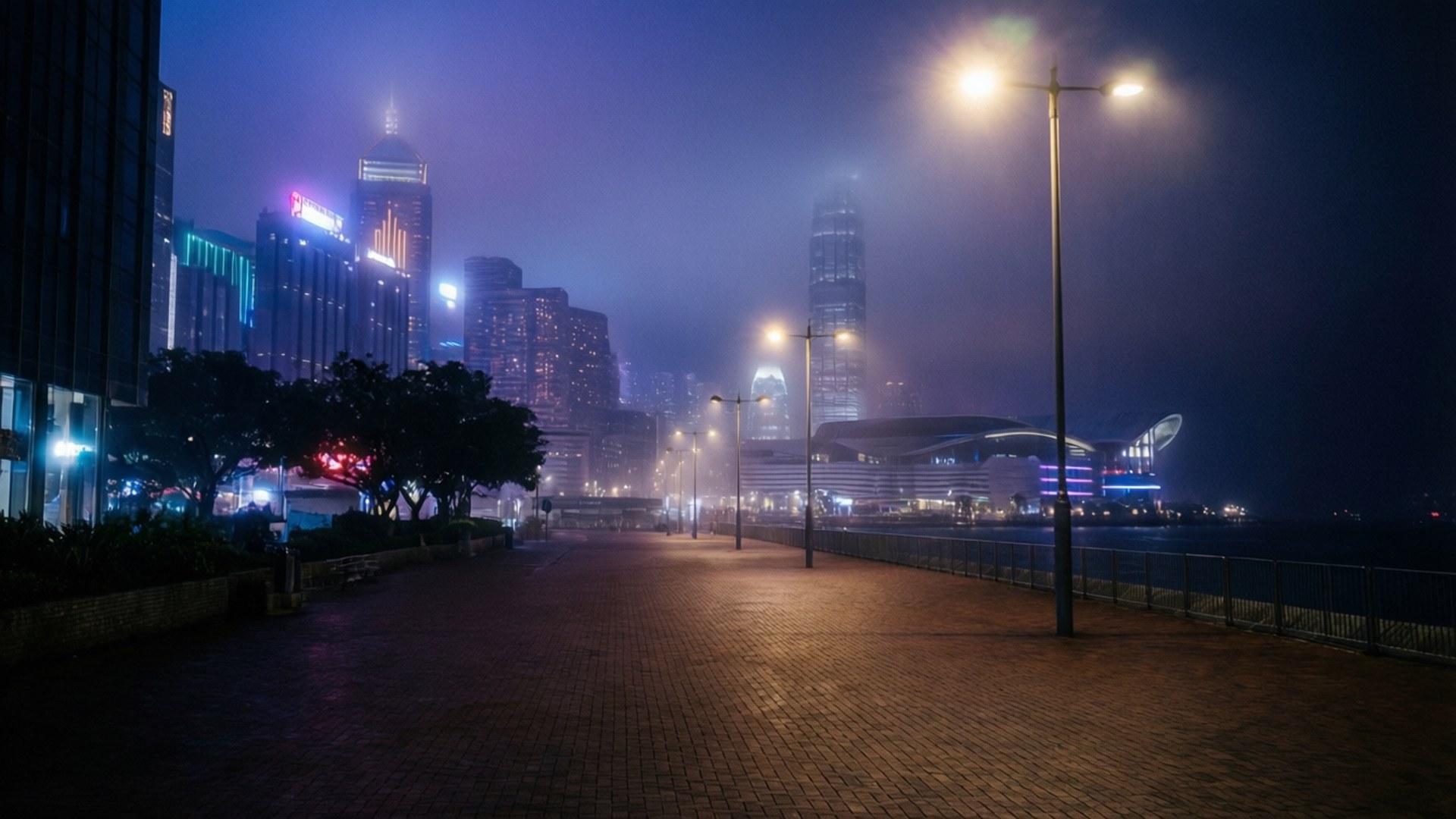 午夜神秘尖沙咀 壁紙 — 霧夜漫步在濕漉漉的磚砌長廊上，閃爍的路燈和背後高聳摩天大樓的朦朧城市天際線。