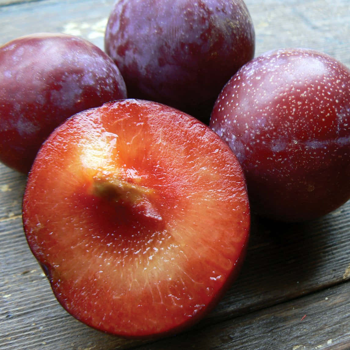 Red Plum 桌布 壁紙 — 半個布冧露出多汁的紅色果肉，旁邊放著完整的布冧，置於經風化的木質表面上。