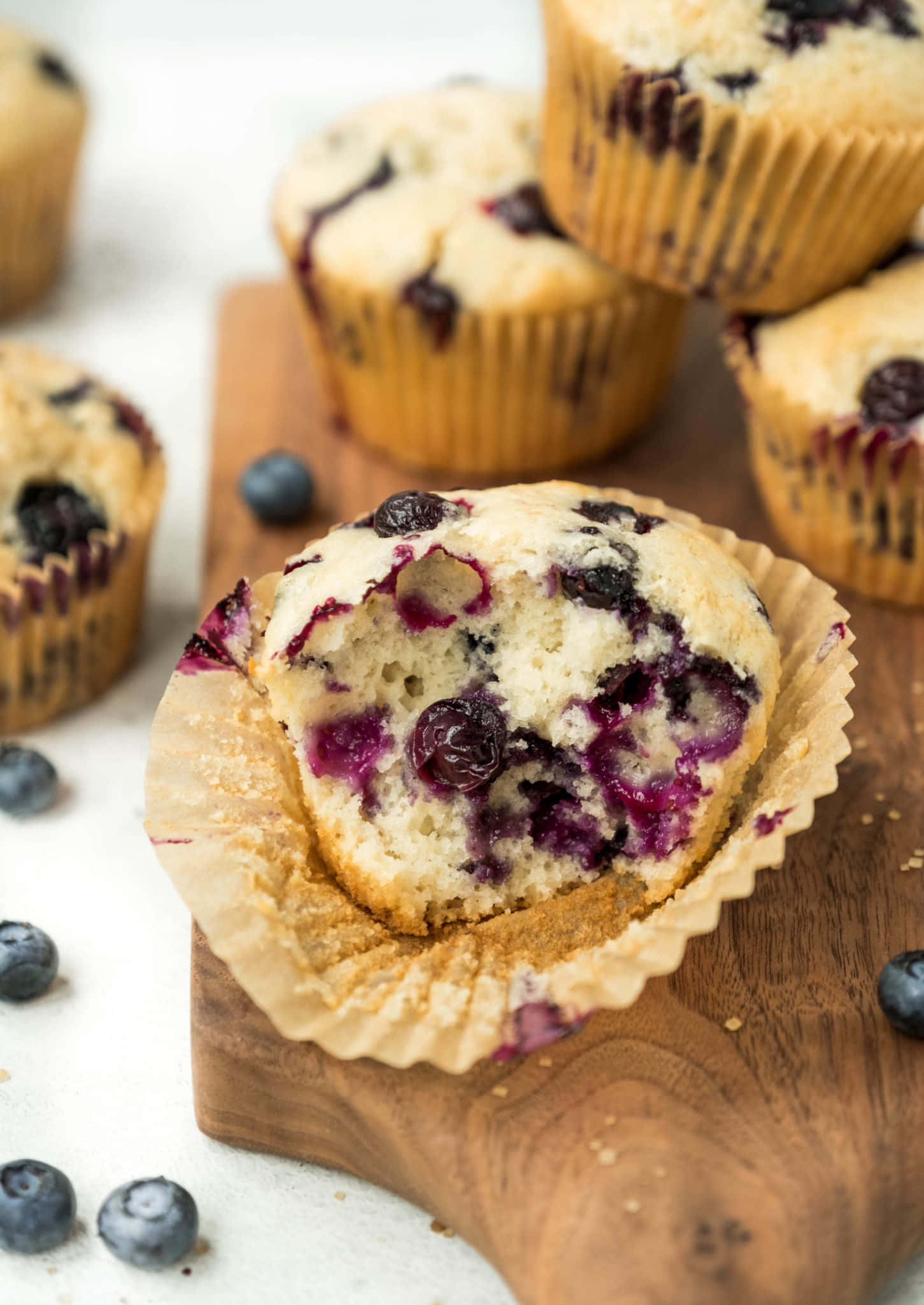 Blueberry Muffins 桌布 壁紙 — 半個藍莓鬆餅的特寫，露出多汁的紫色莓果和柔軟的麵包屑，放在木板上。