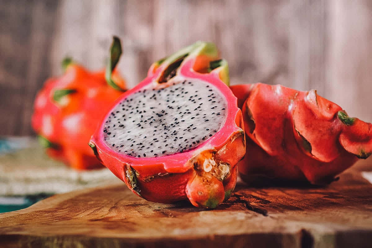 Red Fruit 桌布 壁紙 — 半個鮮艷的火龍果，白色果肉和黑色種子，放在質樸的木板上，旁邊有完整的水果。