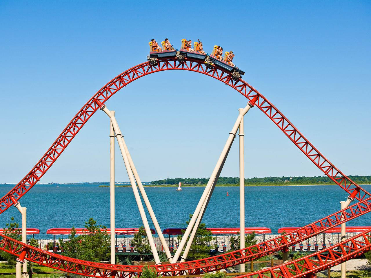 紅色過山車在迴圈頂點，乘客在水上，陽光明媚