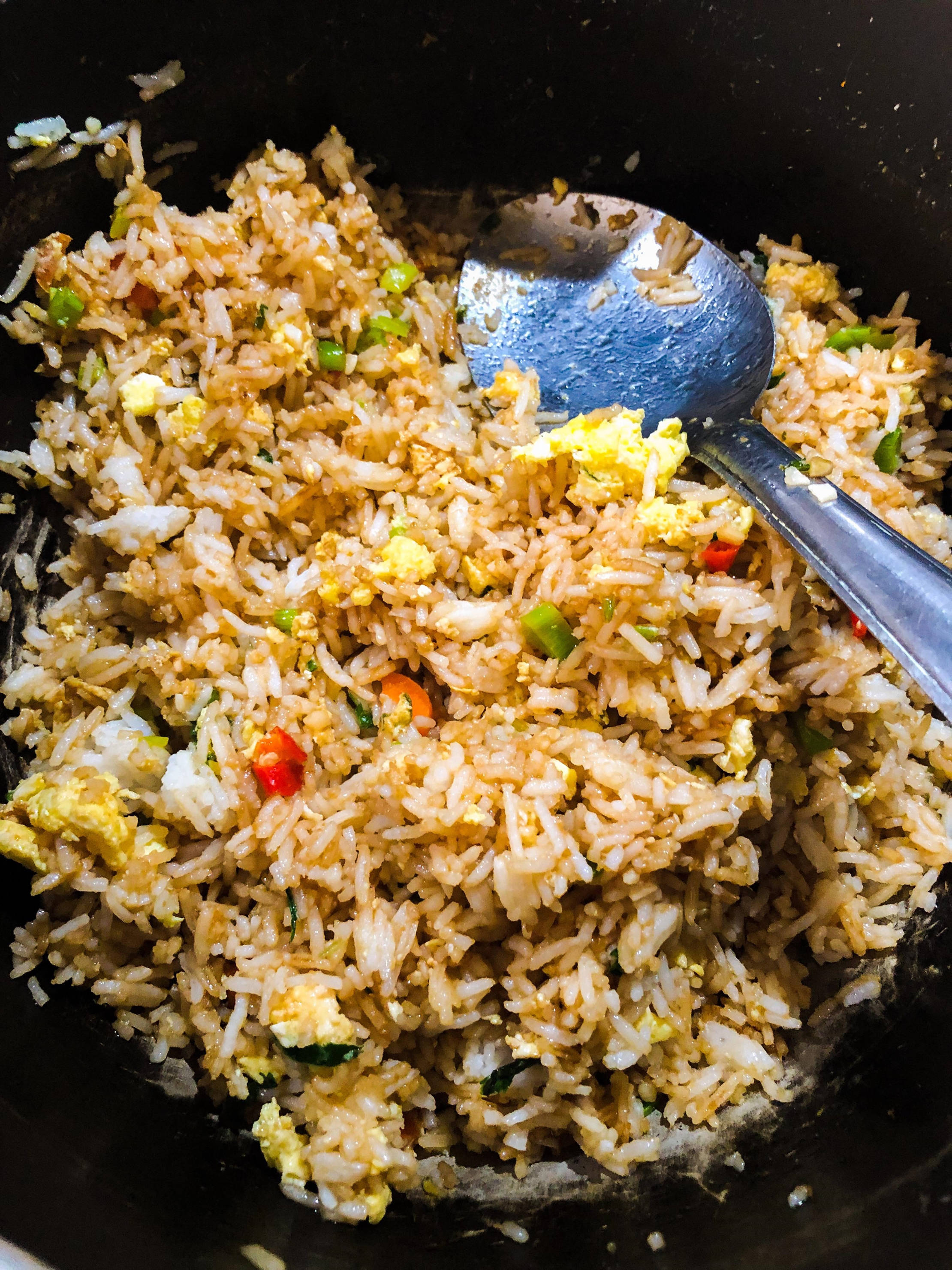 半盤蔬菜炒飯 壁紙 — 金色炒飯配炒蛋和色彩繽紛的蔬菜，放在黑色鑊中，附有金屬匙的特寫。