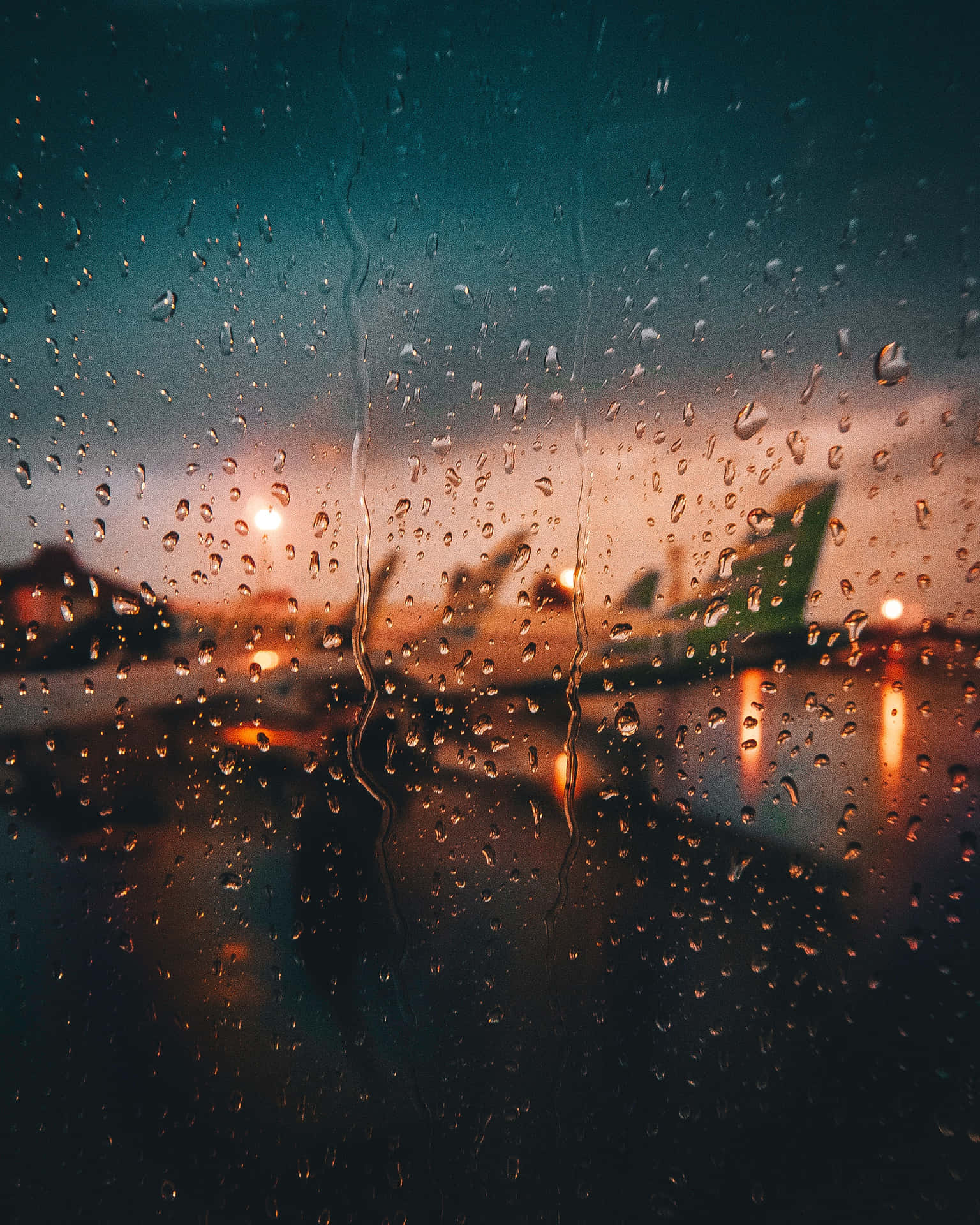 窗戶上的雨滴，俯瞰暮色中的機場飛機。