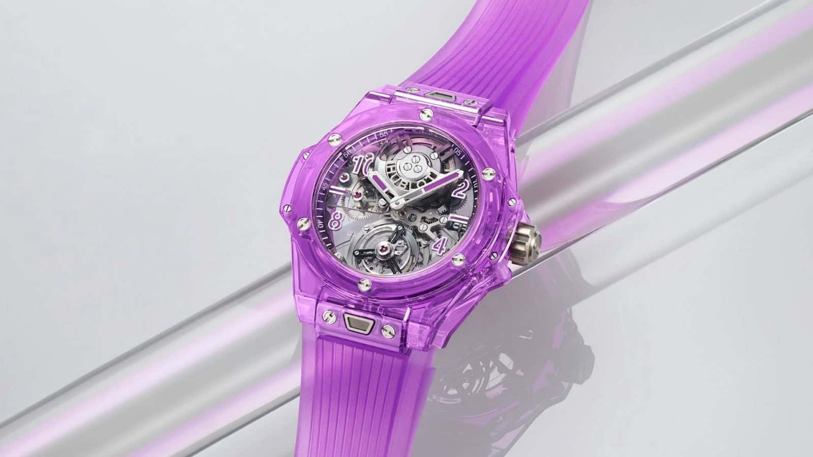 Purple Watch 桌布 壁紙 — 半透明紫色鏤空手錶搭配相配的錶帶，放置在光滑的銀色表面上，露出複雜的內部齒輪。