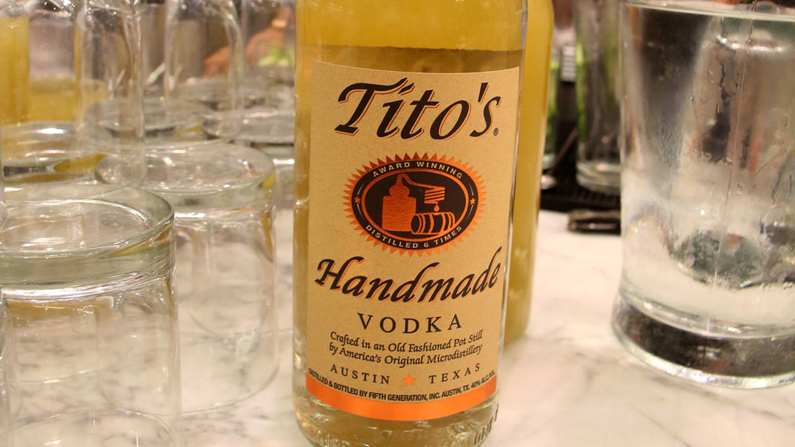 Tito's Handmade Vodka酒瓶放在大理石吧檯上，旁邊有空酒杯
