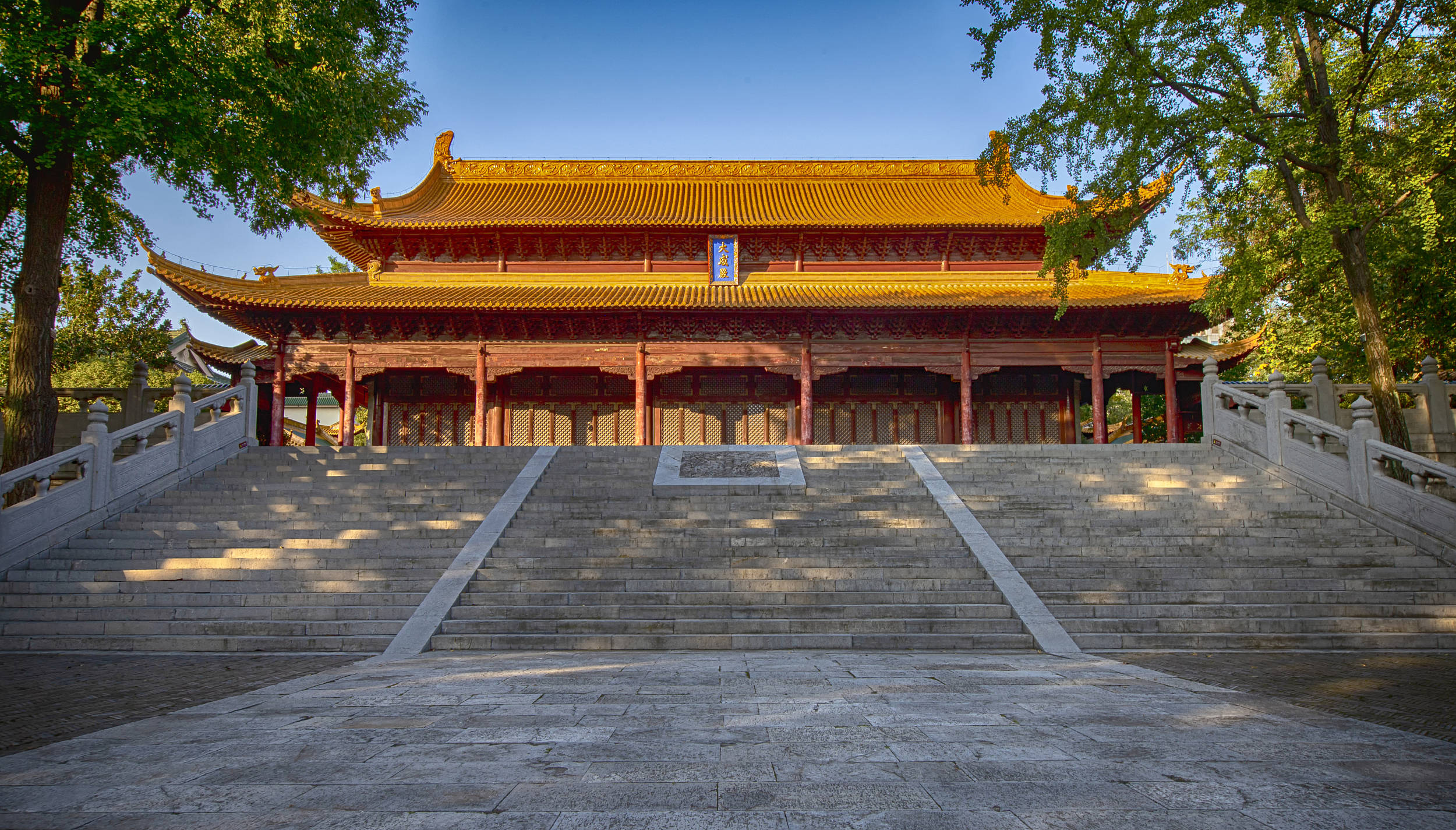 南京博物館外觀 壁紙 — 一座宏偉的傳統中式寺廟，金色屋頂和紅色柱子矗立在寬闊的石階上，上方是清澈的藍天。