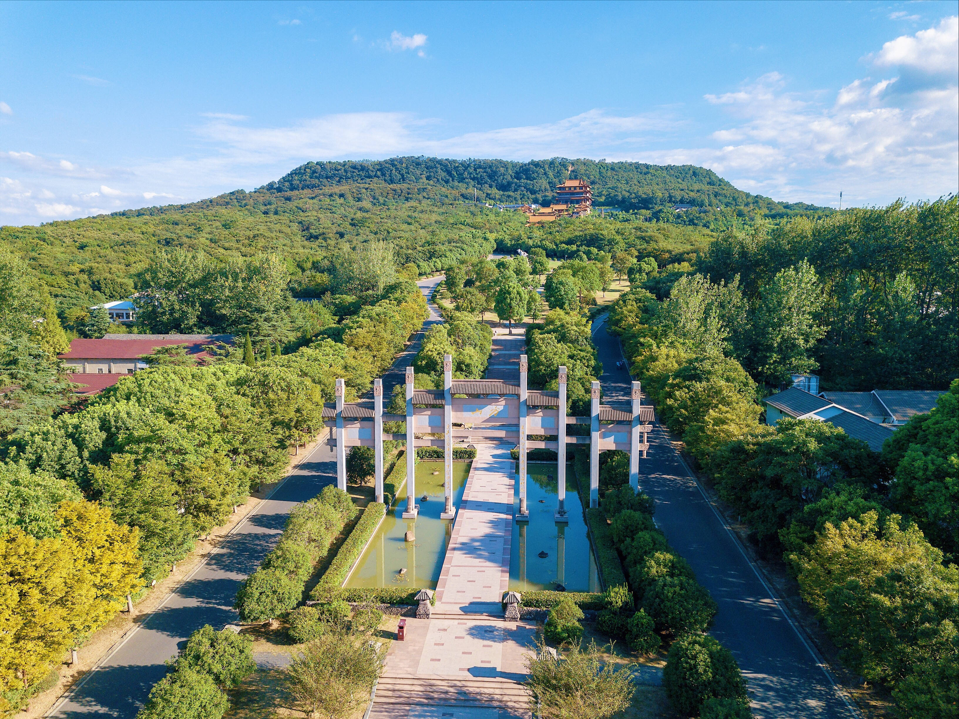 南京方山壯麗風景 壁紙 — 從高空俯瞰，一座宏偉的傳統中式大門兩旁是水道，通往一座位於青翠山頂的寶塔，背景是明亮的藍天。