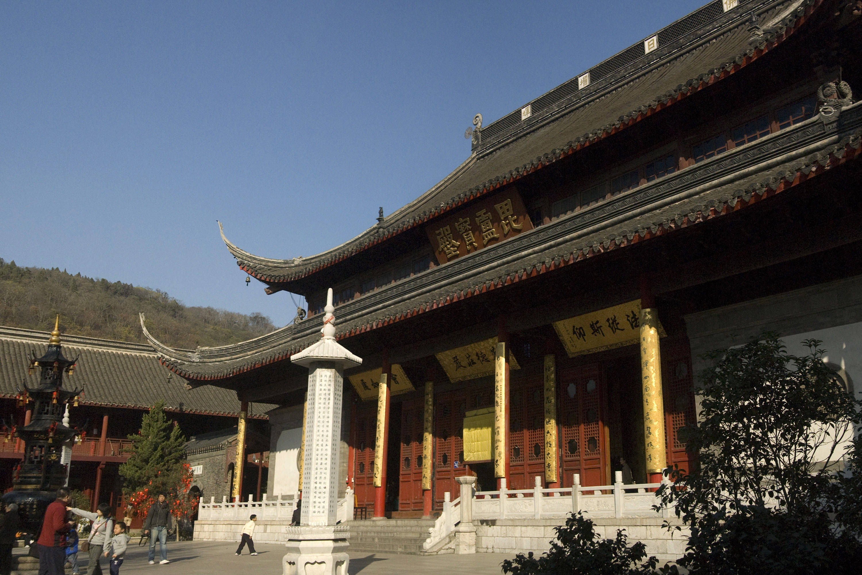 南京栖霞寺 壁紙 — 一座宏偉的傳統中式寺廟，擁有飛簷翹角的瓦頂和紅色柱子，矗立在晴朗的藍天下，遊客在附近走動。