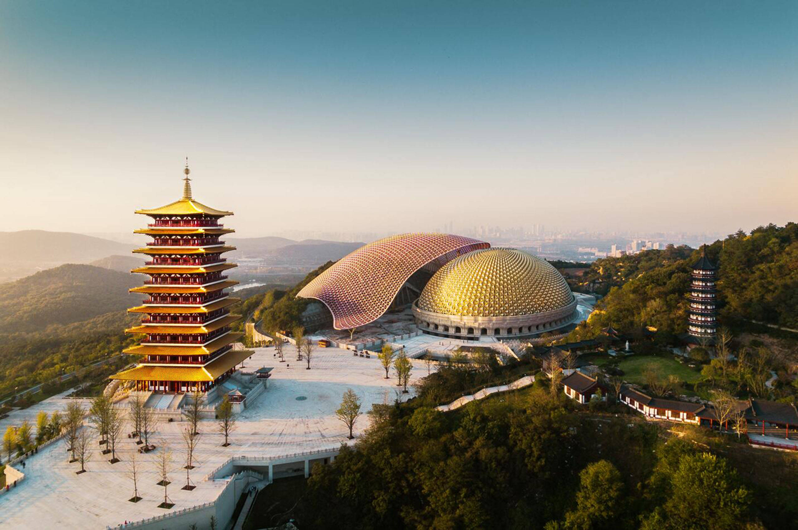 南京牛首山文化公園 壁紙 — 日出時分，金色寶塔和圓頂寺廟建築群坐落在翠綠山丘之間的鳥瞰圖。