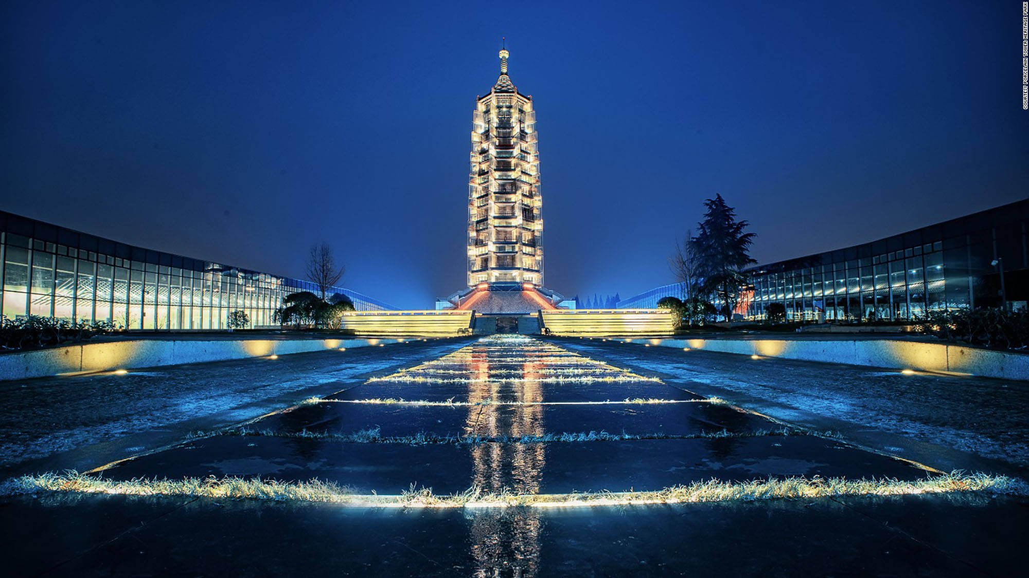 南京瓷塔 壁紙 — 一座高聳的燈光寶塔在夜晚巍然聳立，燈光完美地反射在帶有幾何水景的濕潤廣場上。
