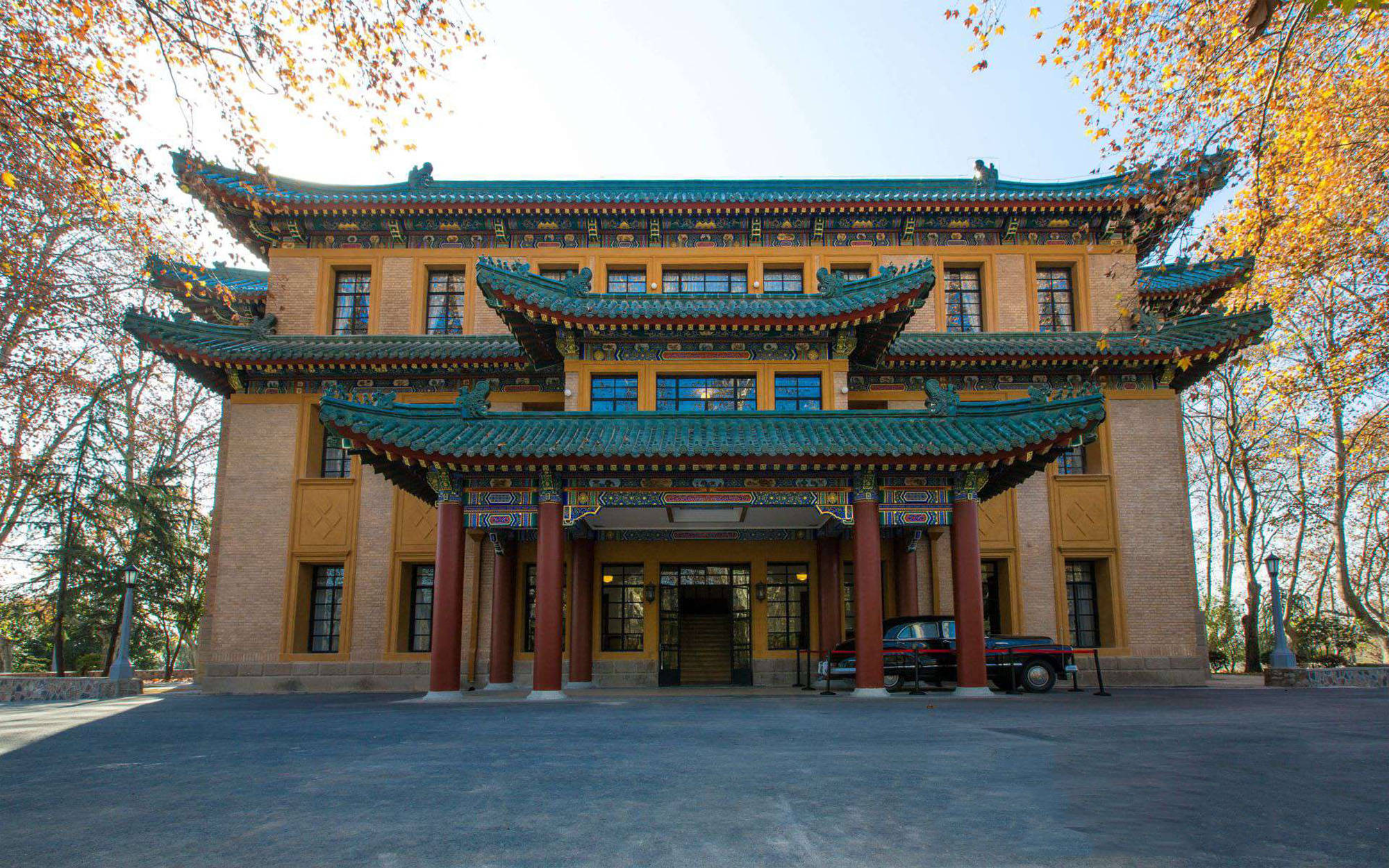 南京美齡宮 壁紙 — 一座宏偉的傳統中式建築，擁有青綠色屋頂和紅色柱子，矗立在秋樹下，樹葉金黃。