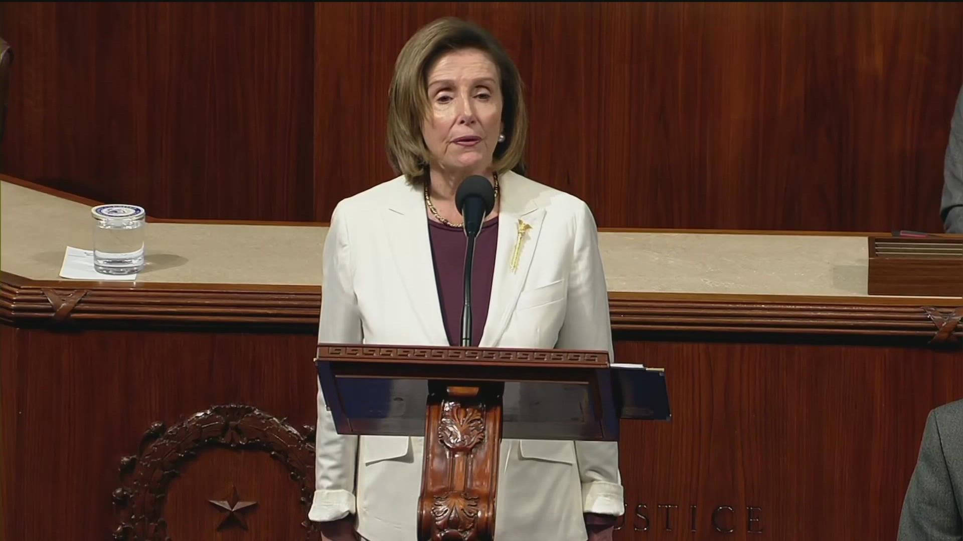南希·佩洛西嚴肅演講 壁紙 — 蘭茜·佩洛西站在正式會議廳的木製講台上發表演講，旁邊放著一杯水。