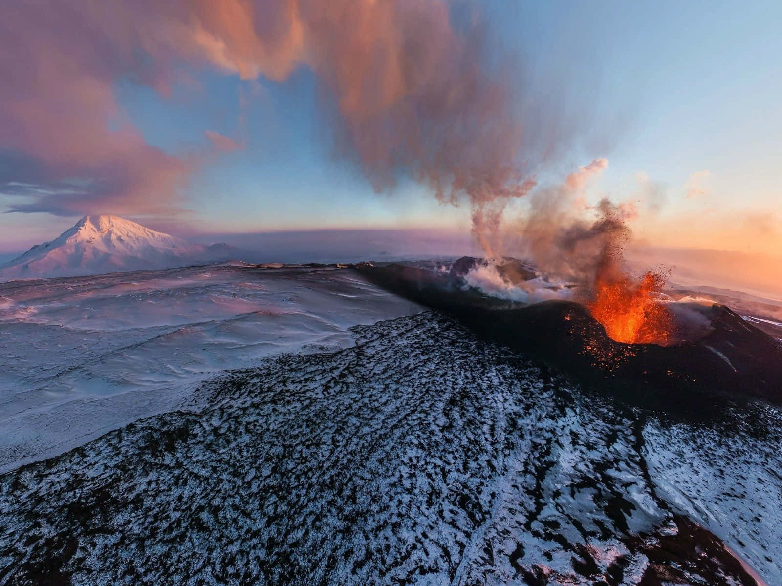 在色彩繽紛的日落天空下，白雪覆蓋的火山噴出熔岩和火山灰。