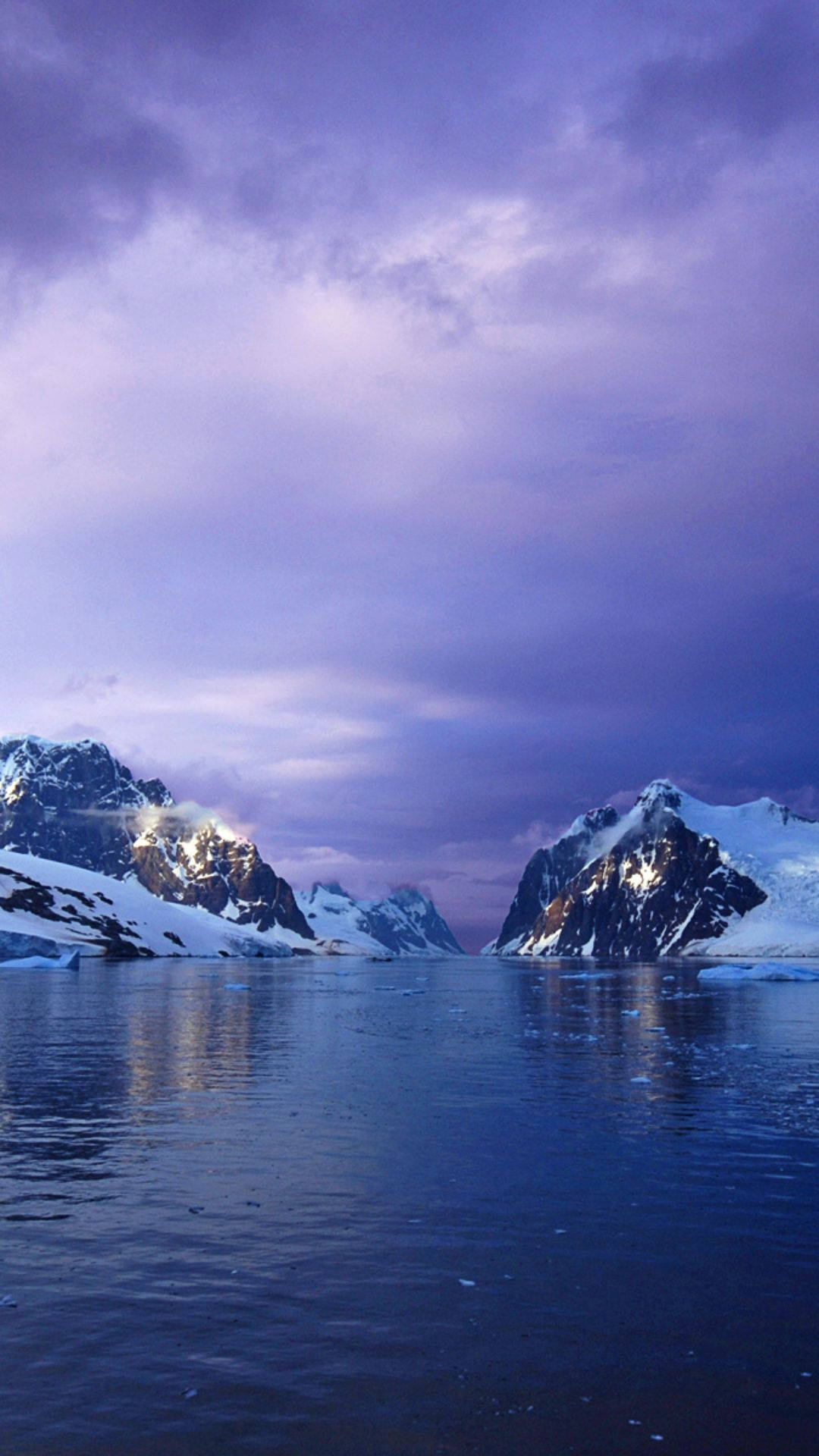 南極洲對峙雙峰 壁紙 — 白雪覆蓋的山峰從冰冷的水域中升起，在戲劇性的紫色暮光天空下。