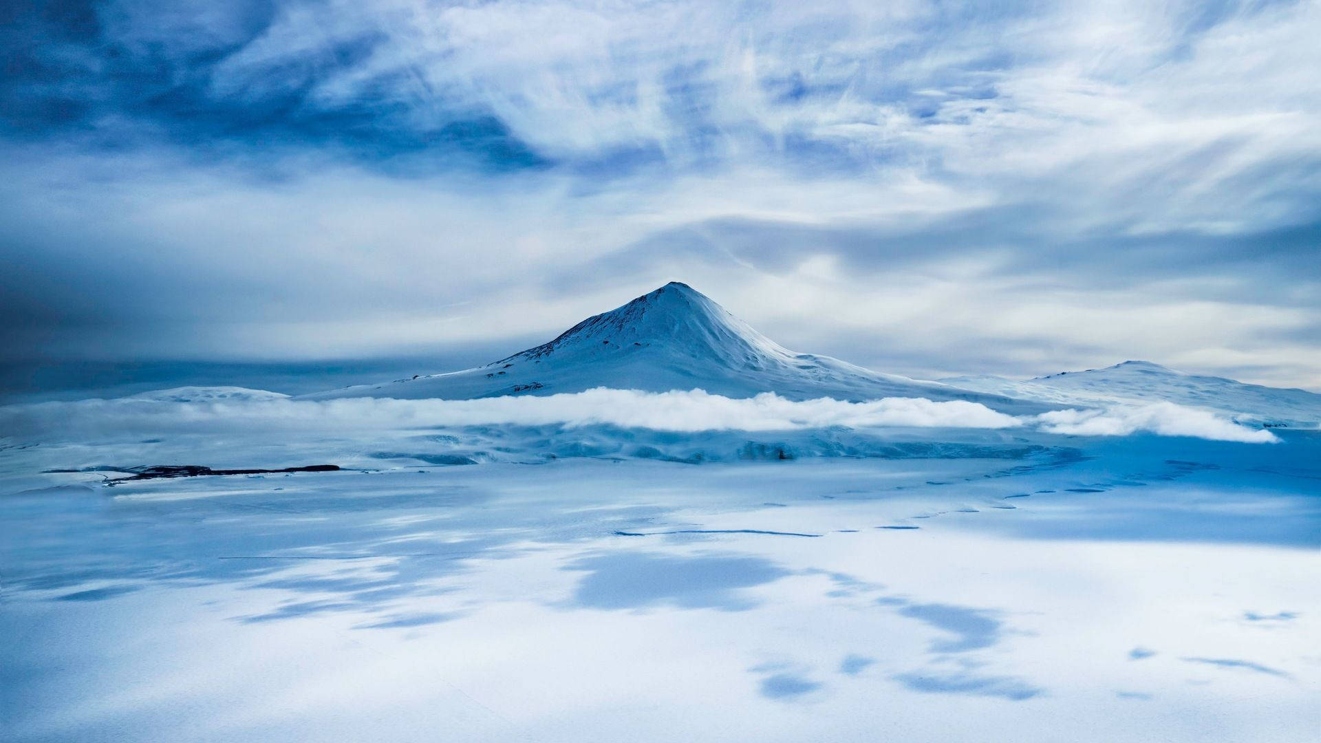 南極洲覆雪山峰 壁紙 — 白雪覆蓋的山峰在戲劇性的藍天下，從廣闊冰封景觀的雲海中升起。