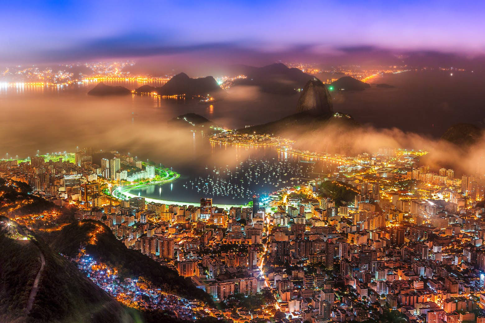 南美洲巴西里約熱內盧夜景 壁紙 — 里約熱內盧黃昏時的鳥瞰圖，城市燈光在霧氣繚繞的山巒和充滿活力的海灣中閃爍。