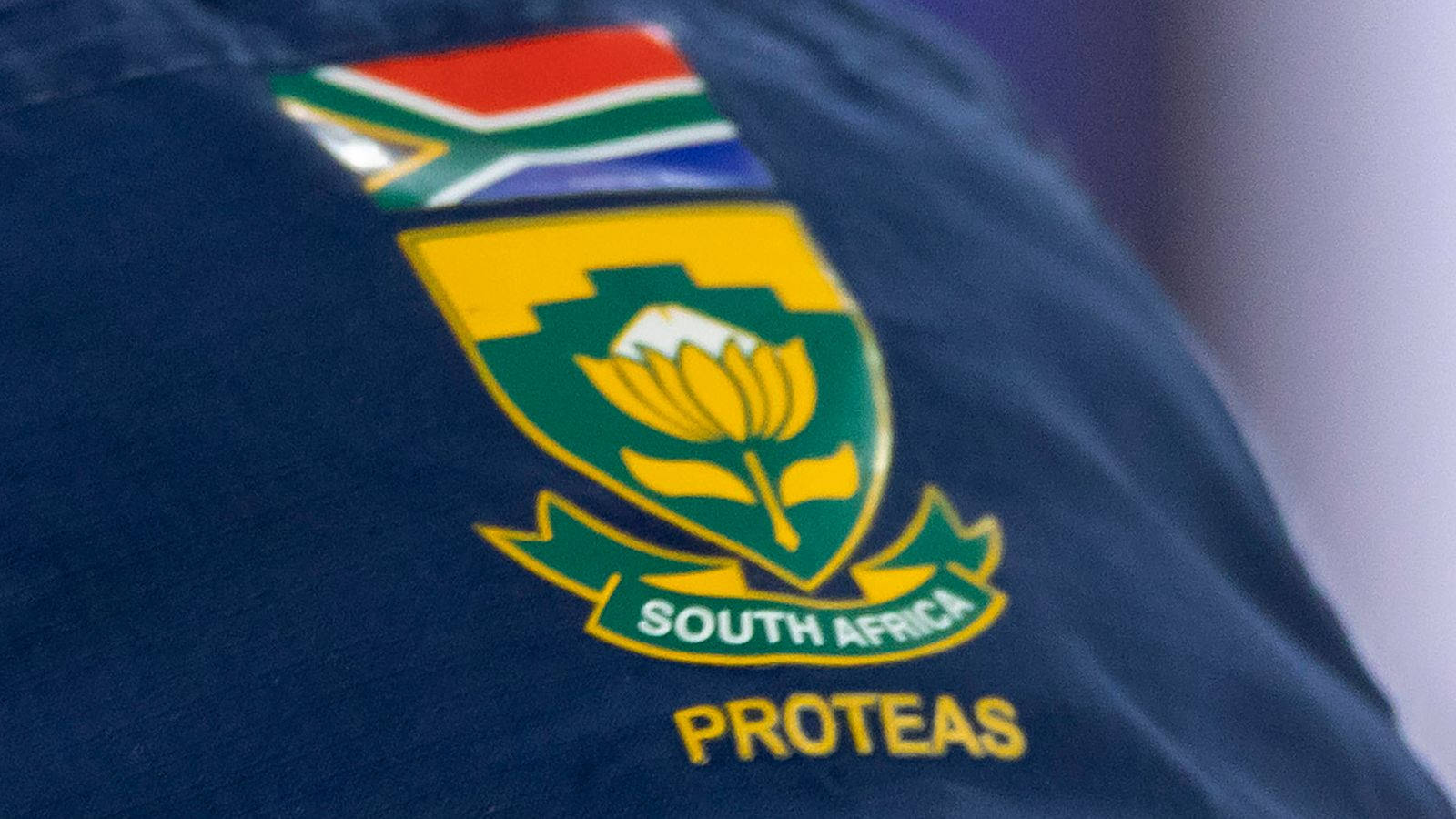 南非板球隊球衣上的標誌 壁紙 — 南非 Proteas 標誌近距離特寫，繡在深藍色布料上，上方有國旗。