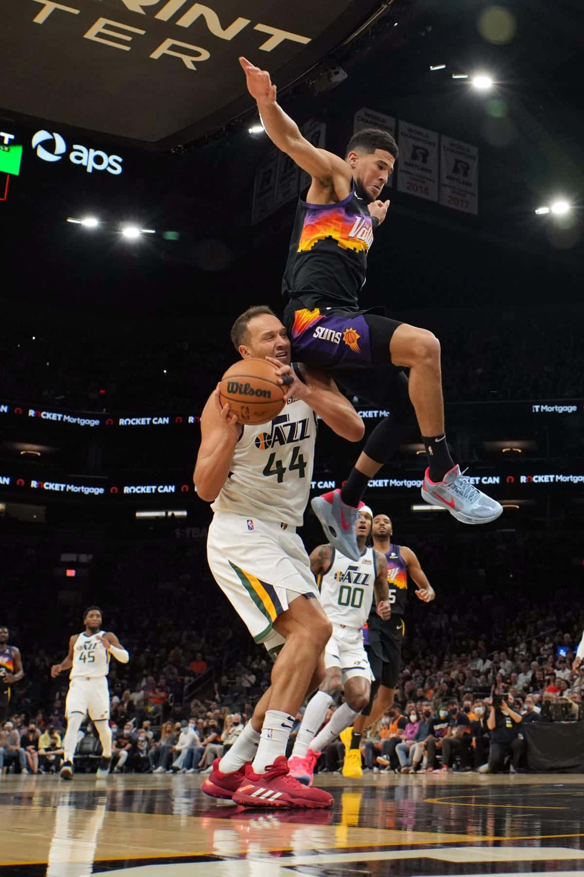 博揚·博格達諾維奇 NBA 烏特ah 爵士隊 壁紙 — 一名身穿白色球衣的籃球運動員跳起封阻投籃，而一名身穿黑橙色球衣的對手則高高躍起準備入樽。