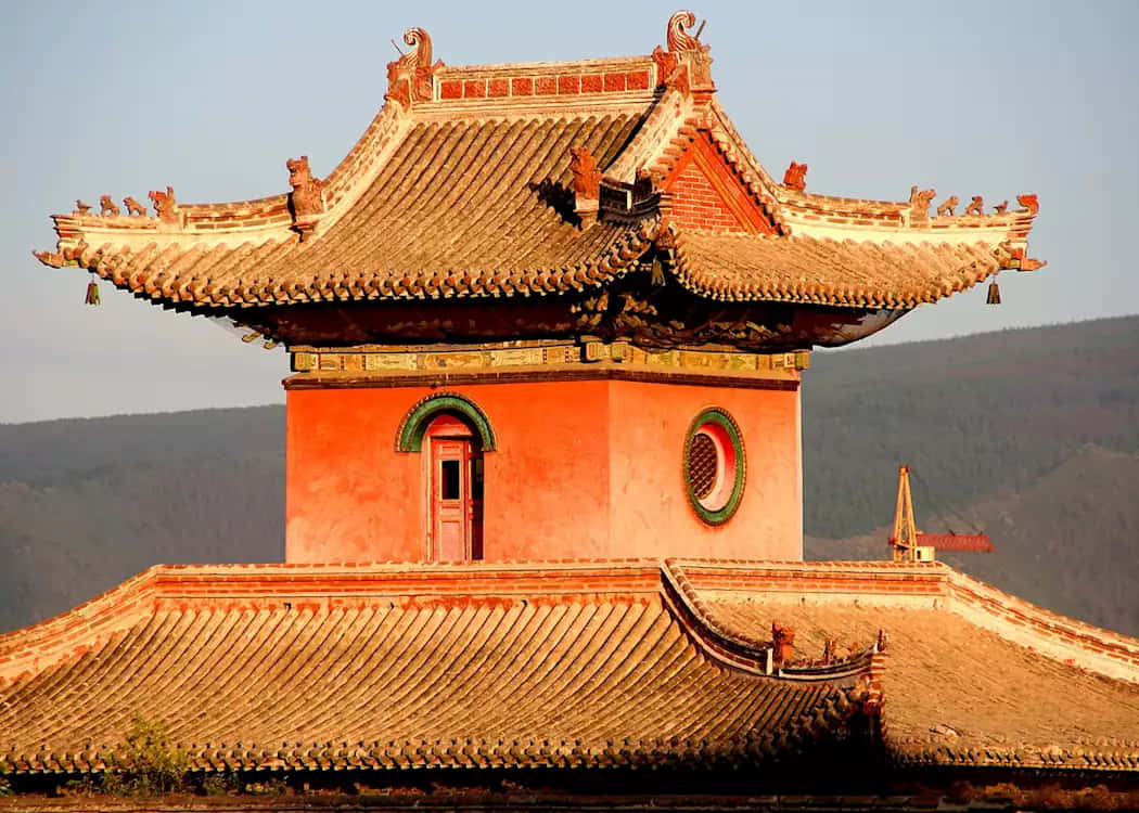 古老的中國寺廟塔樓，彎曲的屋頂和紅牆，映襯著日落時分的山巒。