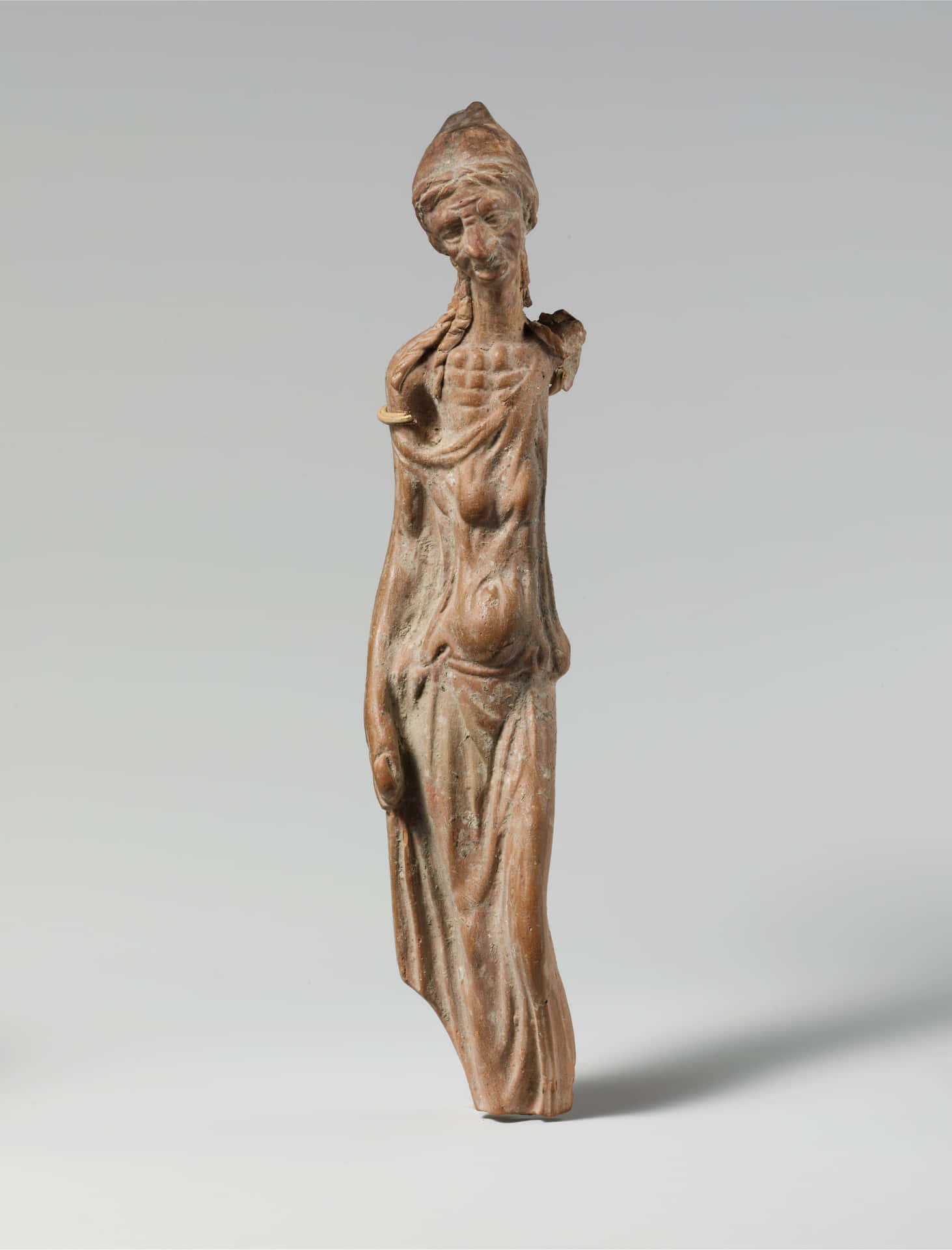 古代赤陶雕像，一位身披垂褶布料的女性側面站立。