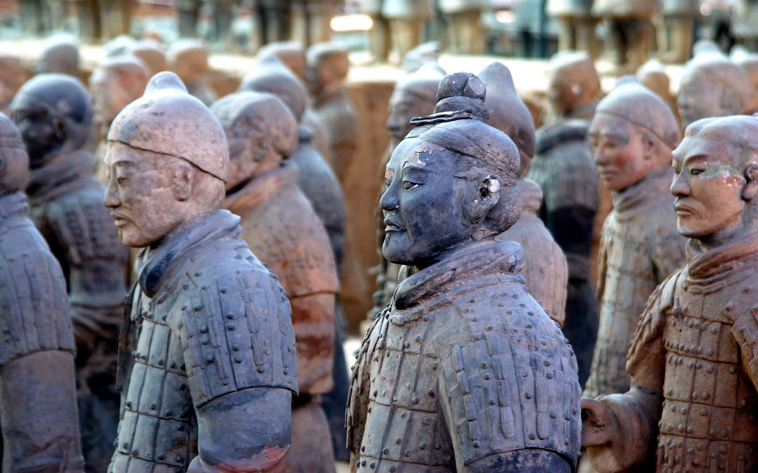 博物館外的秦俑雕塑展示 壁紙 — 一排排古老的兵馬俑在柔和日光下整齊排列，細節豐富的盔甲和風化的表情顯得莊嚴肅穆。