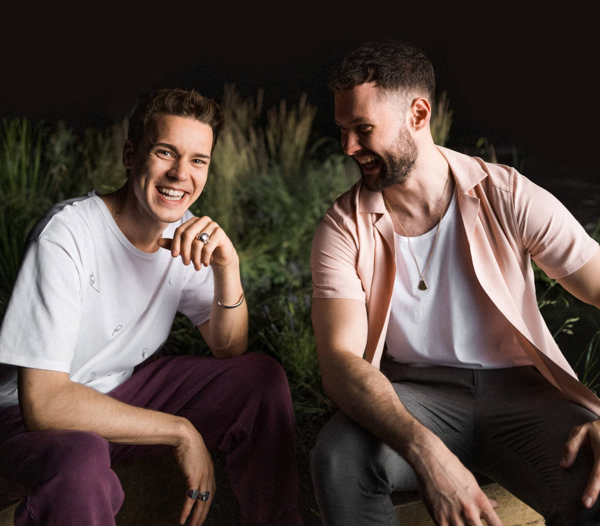 卡勒姆·斯科特與Felix Jaehn 壁紙 — 兩個微笑的男人在戶外夜晚被高大的綠色植物包圍，分享歡樂的時刻。