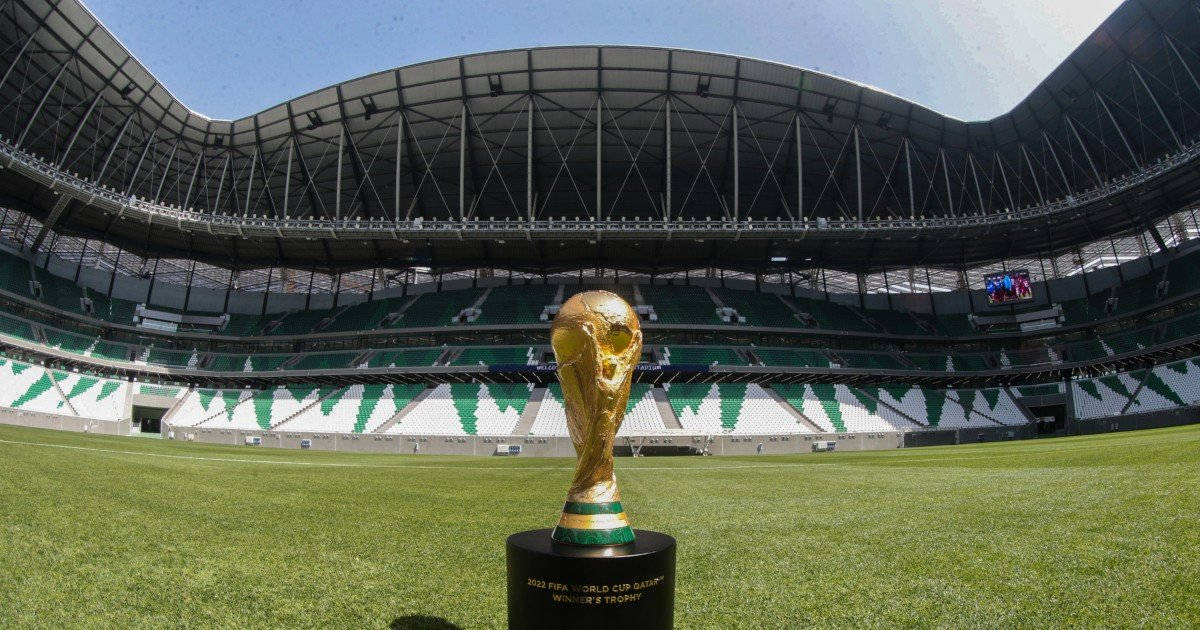 卡塔爾2022世界盃冠軍獎盃 壁紙 — 金色的FIFA世界盃獎盃在晴朗藍天下，矗立於廣闊空蕩體育館內充滿活力的綠色球場中央。